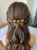 Peineta dorada con flores rojas colocada en el cabello, vista trasera