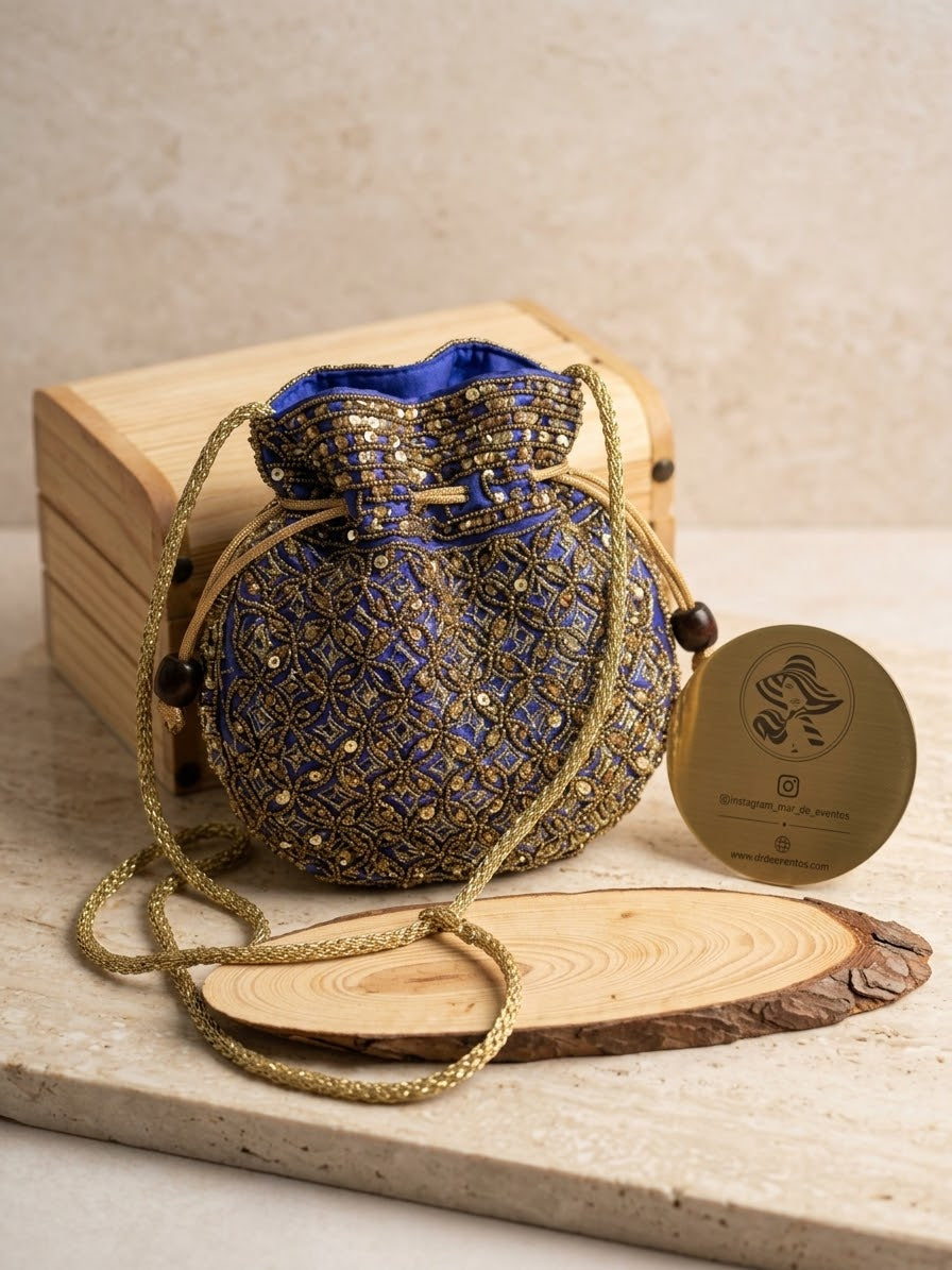 Bolso redondo de tela azul con bordados dorados y cordón de cierre.