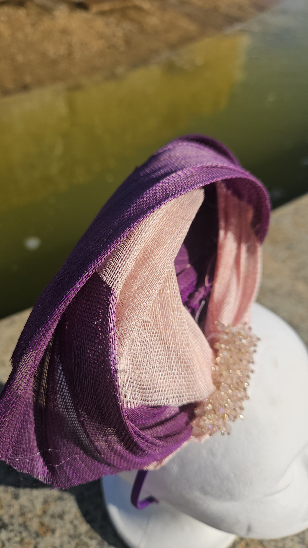 Tocado morado con malla beige y adorno dorado en un tocador lateral sobre maniquí