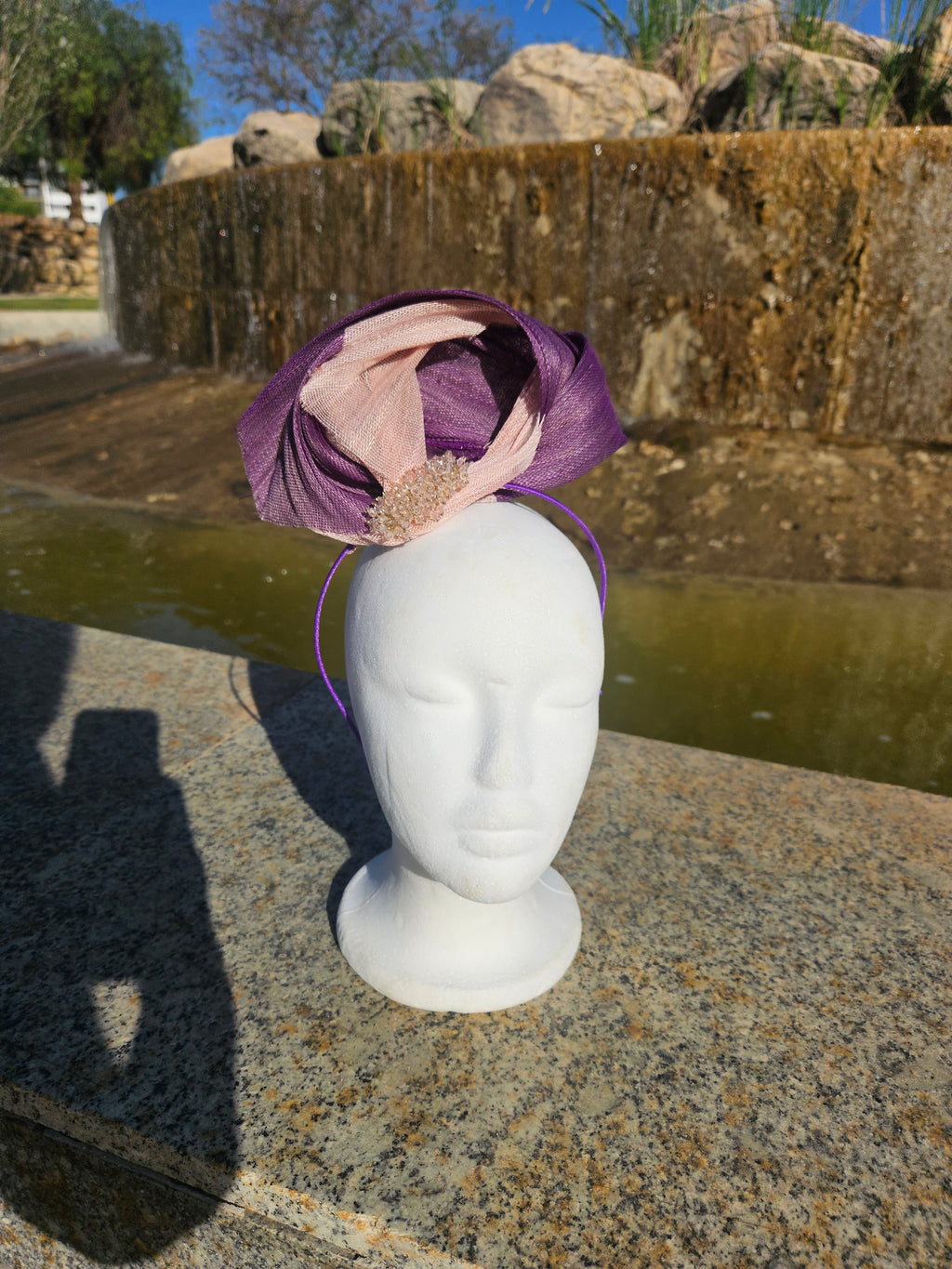 Tocado morado tipo cofia con malla beige y adorno dorado, con lazo en maniquí