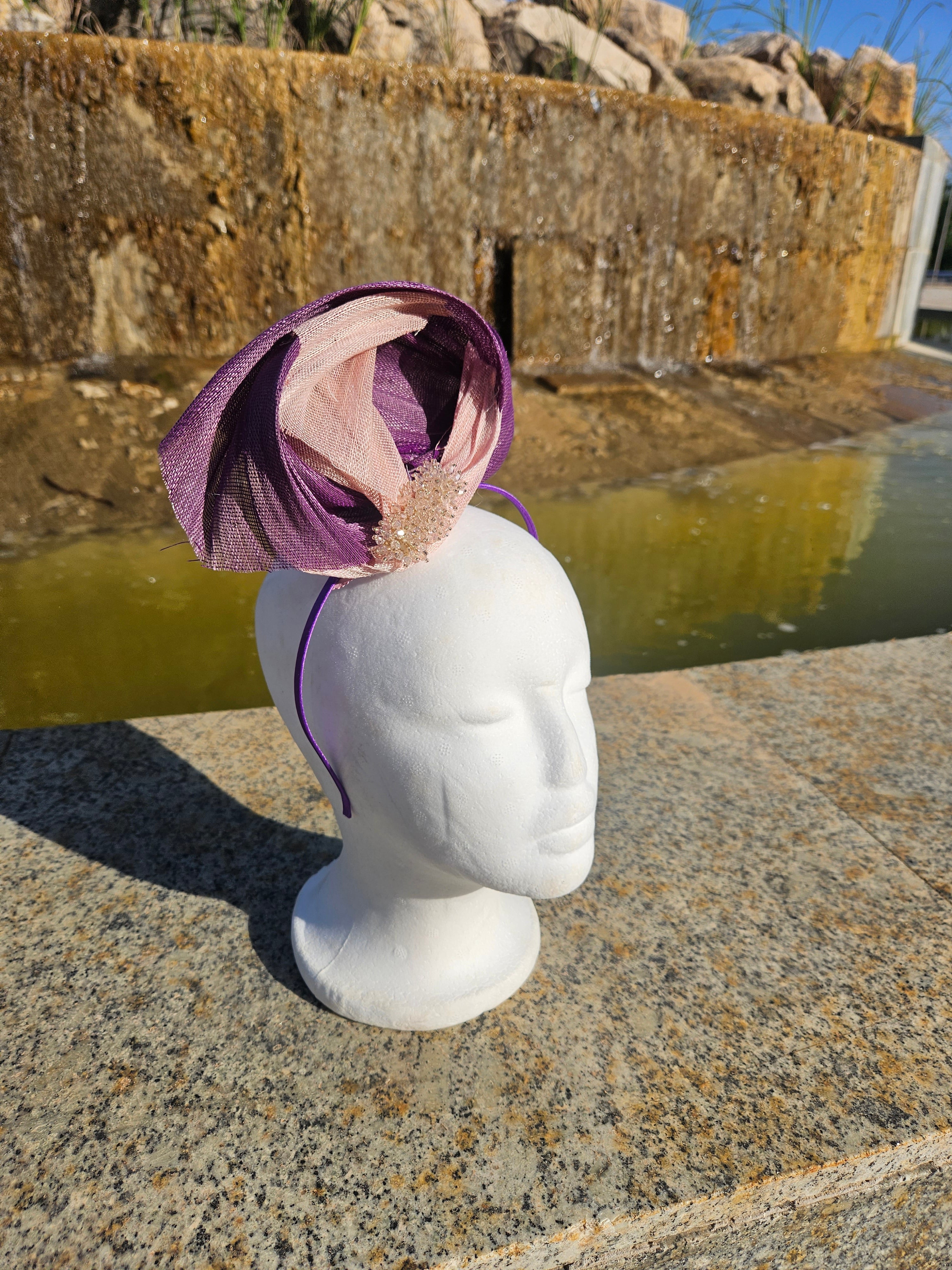 Tocado morado drapeado con malla beige y adorno dorado, visto de lado sobre maniquí
