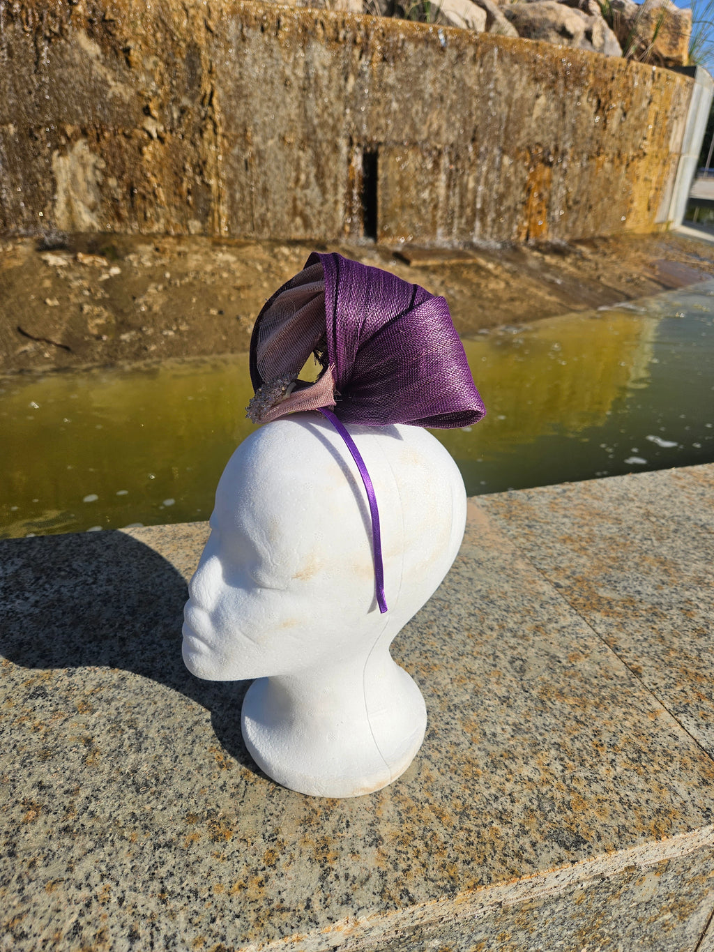 Tocado morado con lazos largos y malla beige, con adorno dorado sobre maniquí