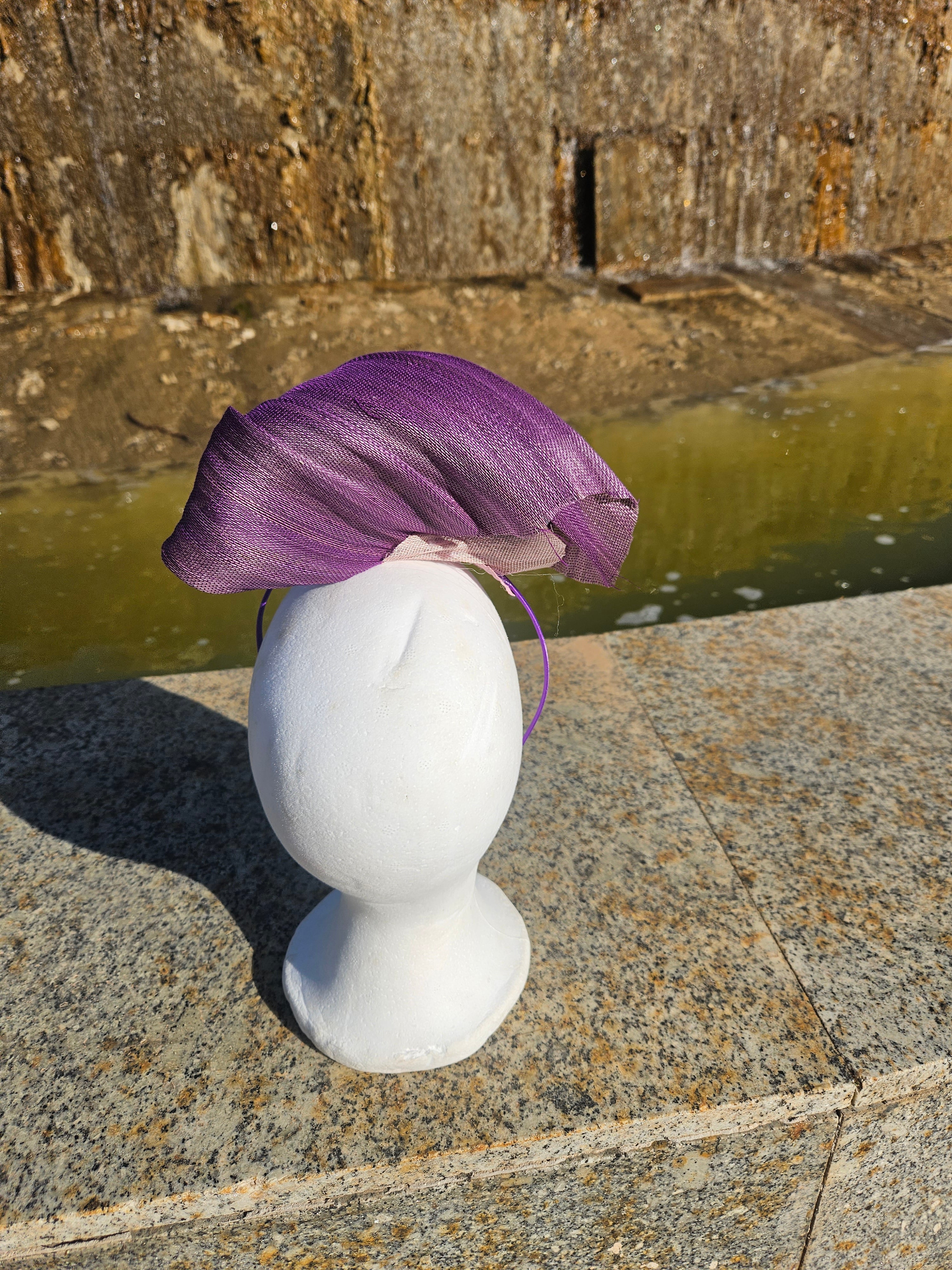 Tocado morado drapeado estilo fascinator sobre la cabeza, con malla beige y adorno dorado