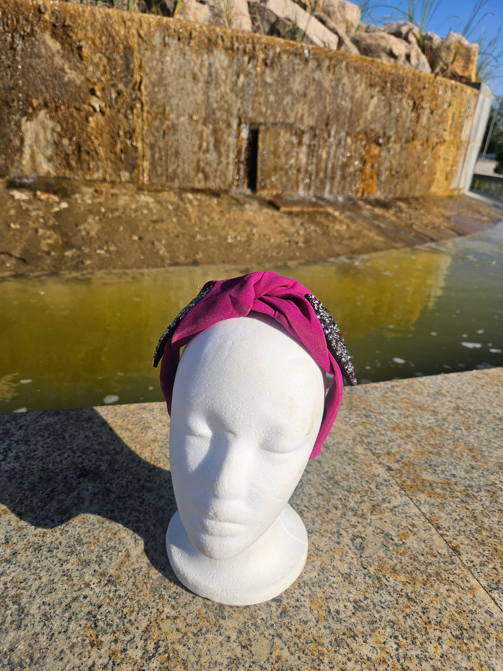 Diadema con lazo fucsia y adorno oval negro con pedrería brillante
