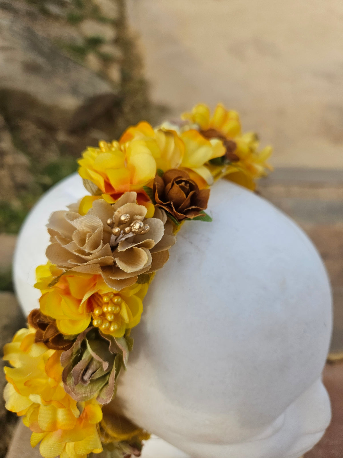 Diadema floral amarilla con flores grandes y detalles marrones, sobre maniquí