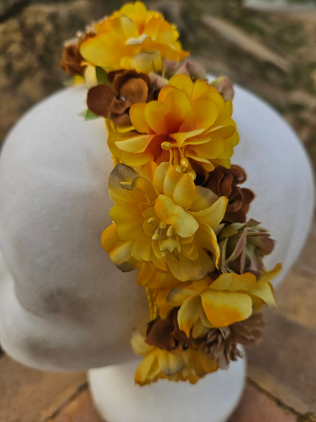 Diadema floral amarilla con flores y hojas marrones, vista frontal sobre maniquí