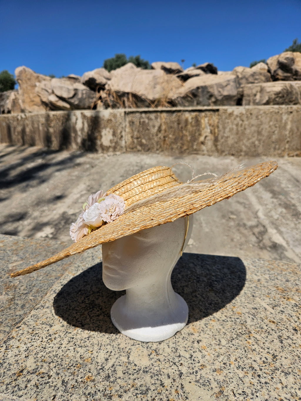 Sombrero de paja beige con flor rosa y ala ligeramente levantada, vista lateral