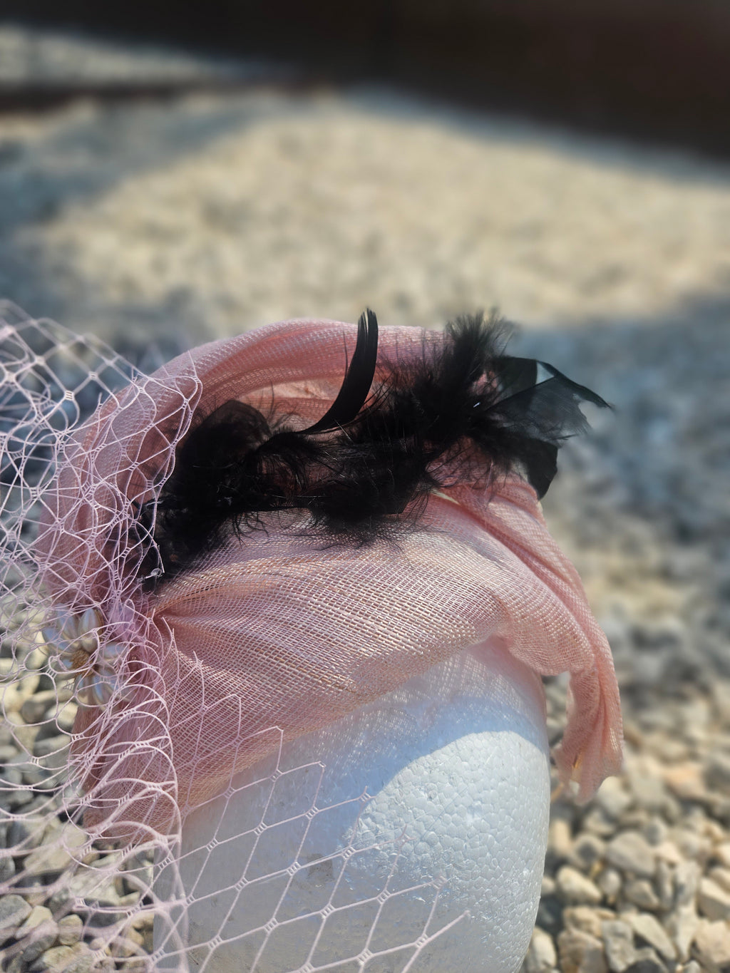 tocado Nandama rosa con pluma negra y velo de tul en diagonal