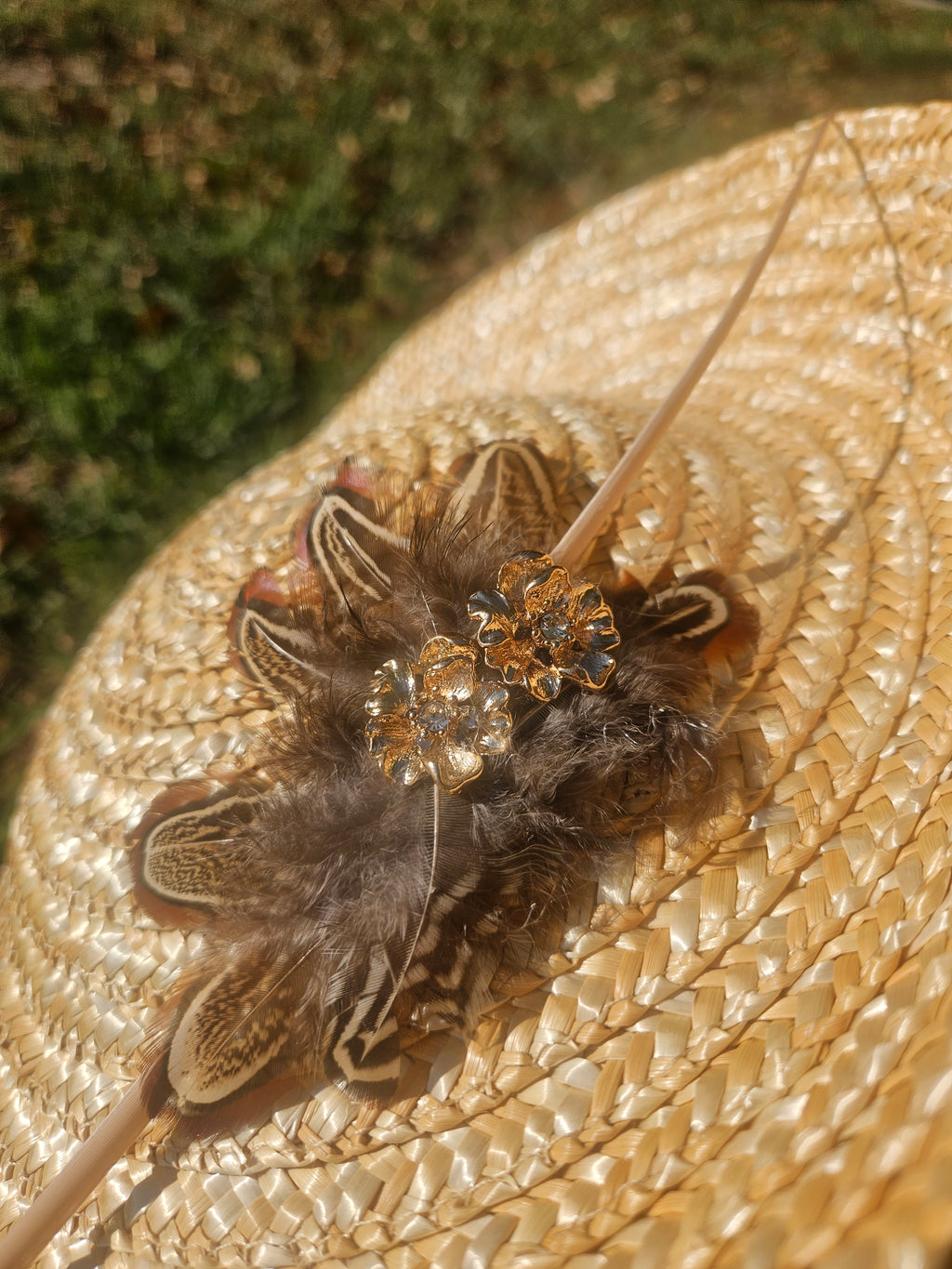 Detalle del tocado del sombrero: flor dorada y plumas sobre rafia beige