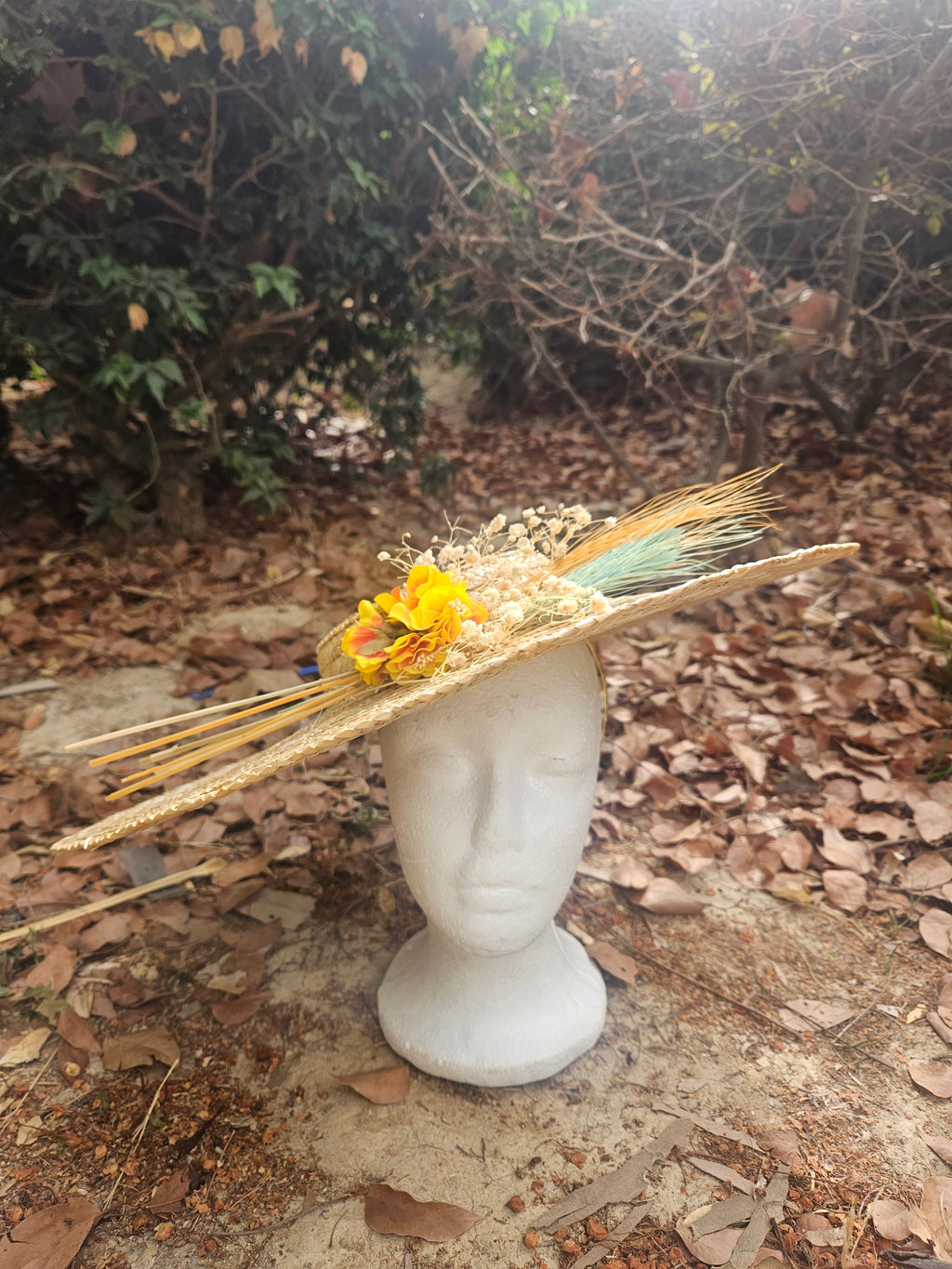 Sombrero de paja beige con flores amarillas y tiras turquesa sobre maniquí blanco