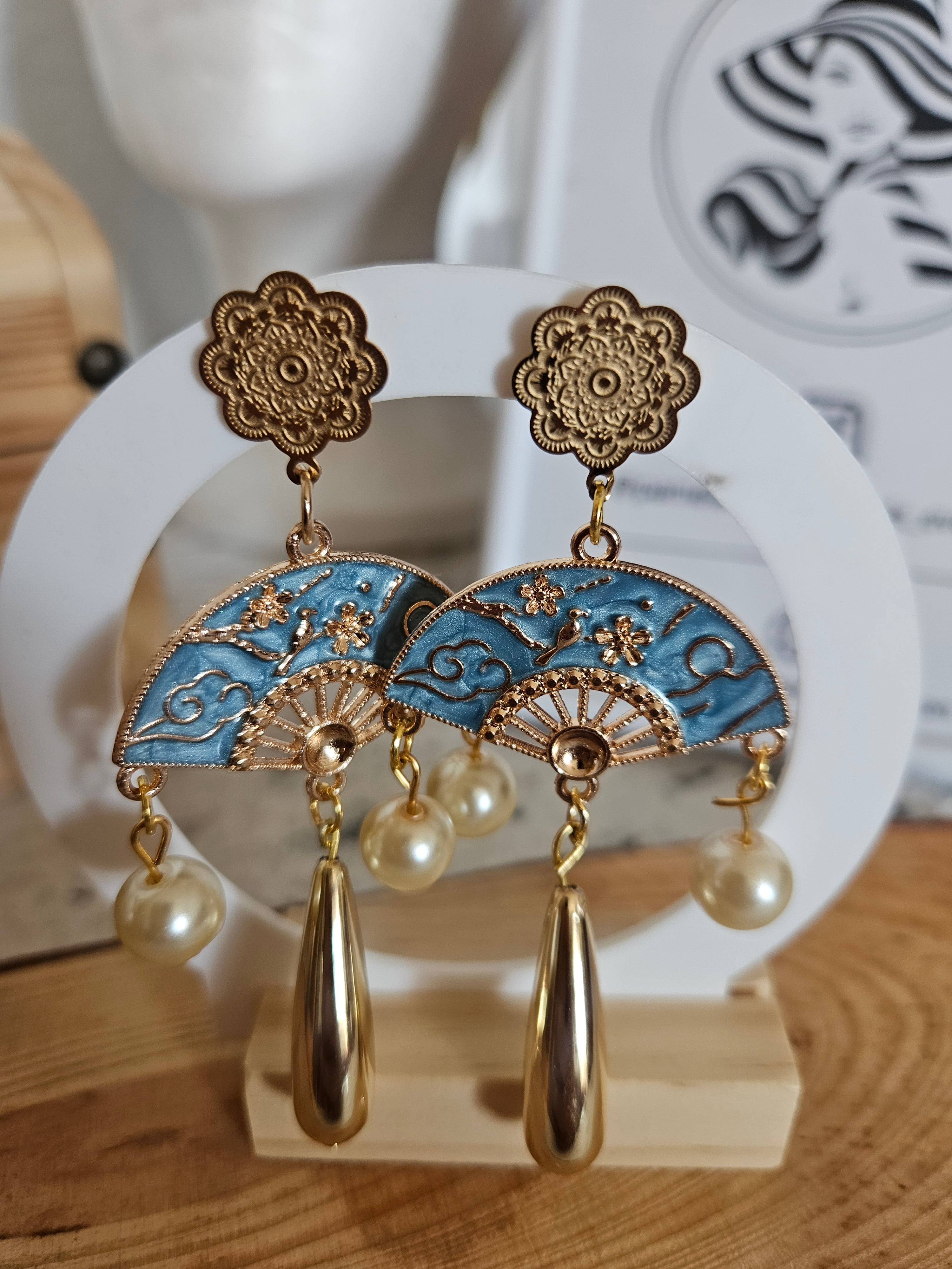 Pendientes dorados con círculos azules tipo abanico, decoraciones doradas y perlas.