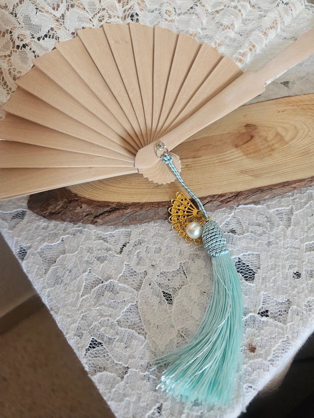 Abanico de madera beige con encaje blanco y borla turquesa con adorno dorado y perla