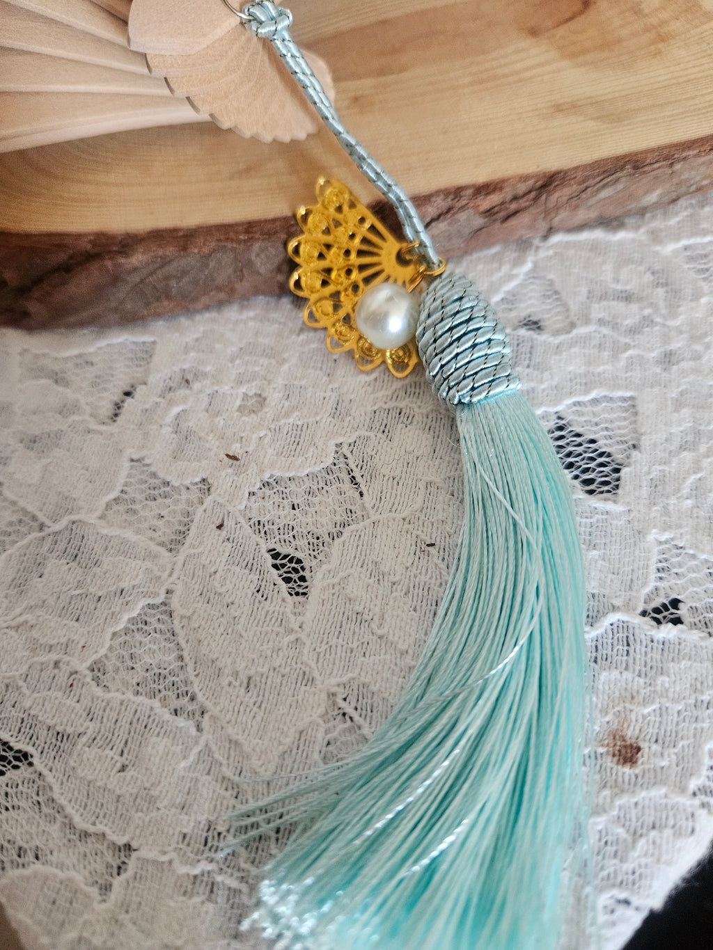 Abanico beige con varilla azul y borla turquesa; detalle dorado con perla en el centro