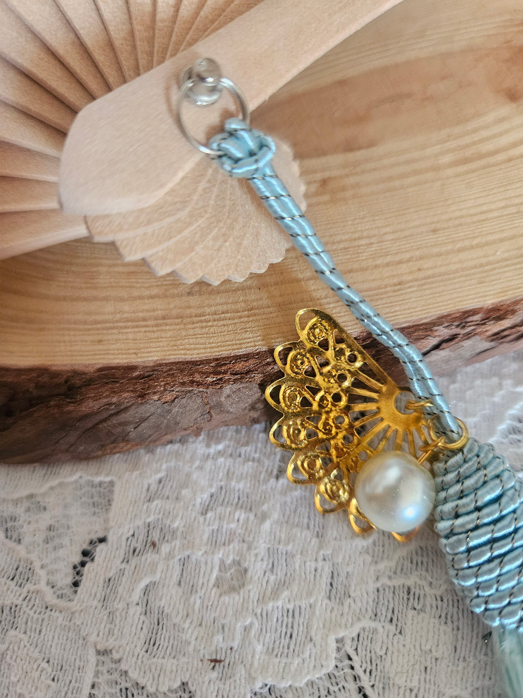 Abanico beige con agarre plateado y cordón azul; adorno dorado floral y perla