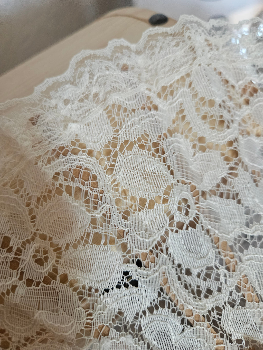 Encaje blanco con motivo floral sobre tela clara, con pedrería brillante en la parte superior