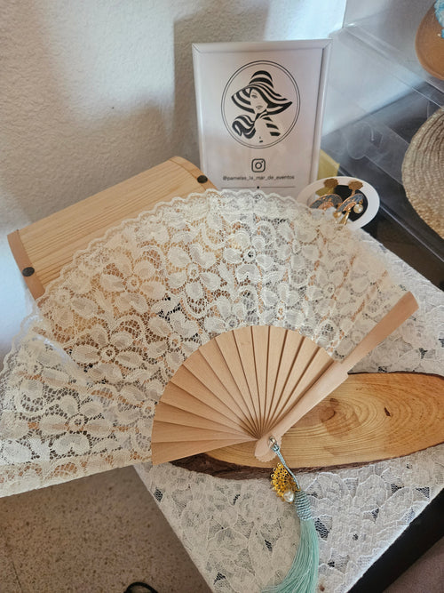 Abanico beige con encaje blanco y borla turquesa; detalle dorado con perla