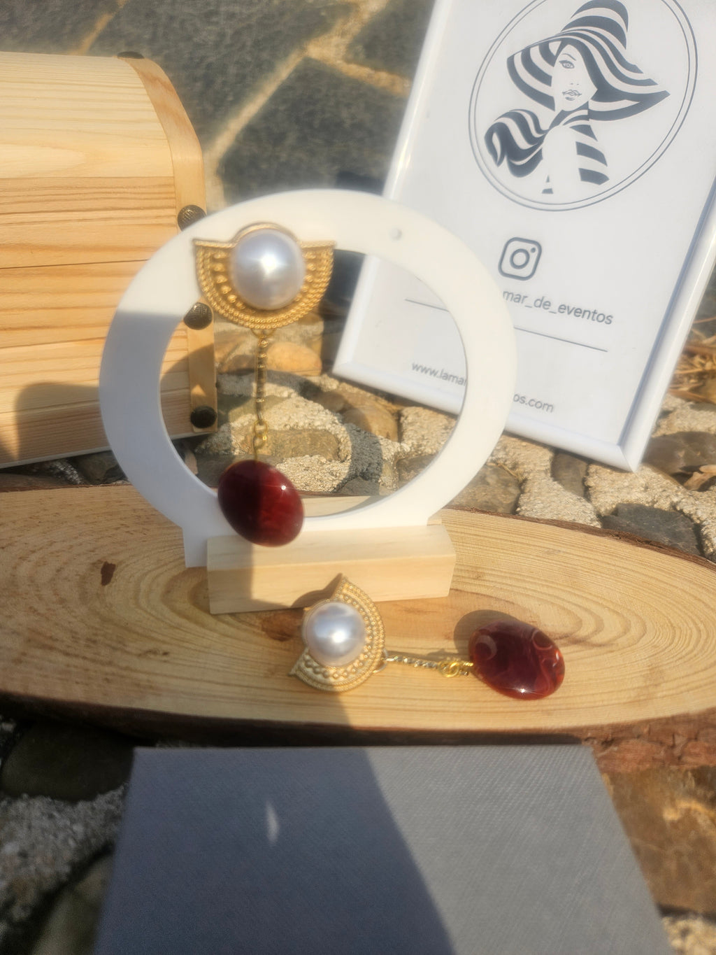 Pendientes colgantes con perla blanca y gota roja en soporte de madera.