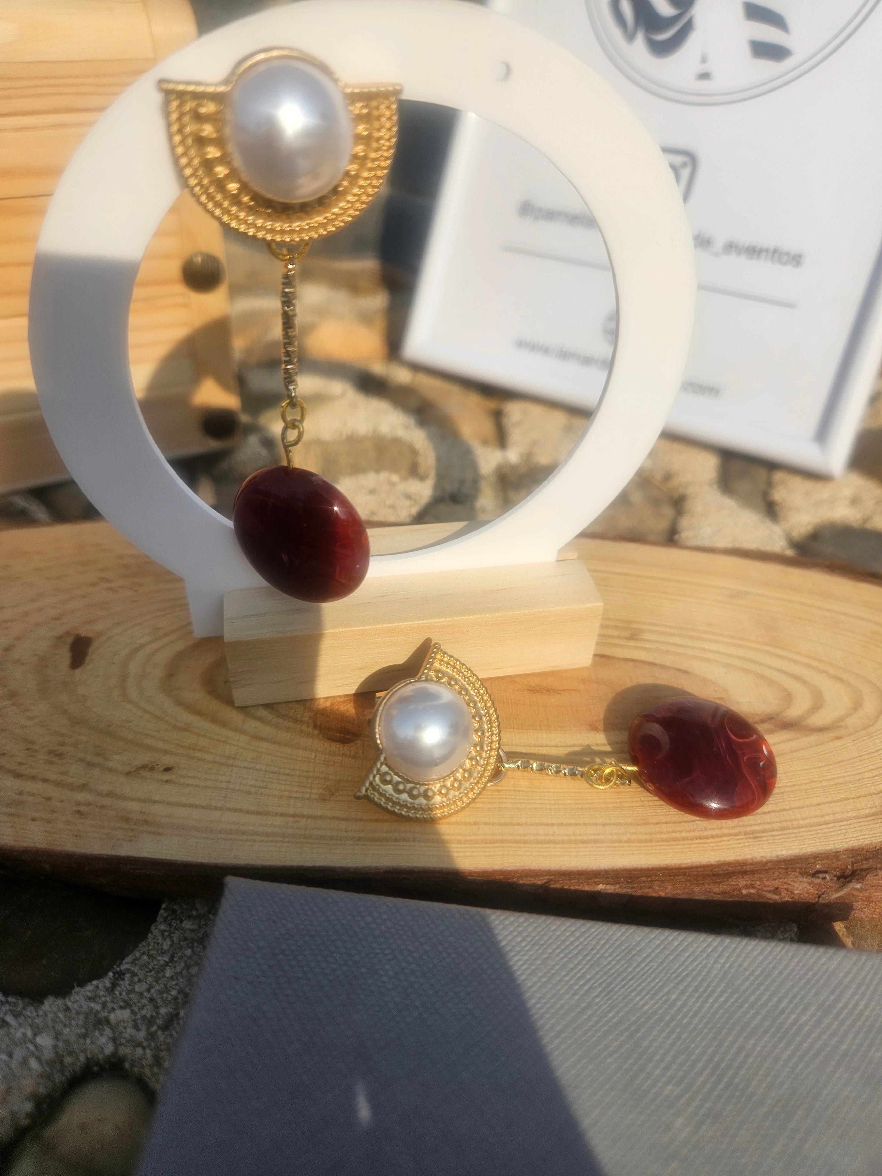 Pendientes colgantes con perla blanca y gota roja, estilo dorado, en soporte.