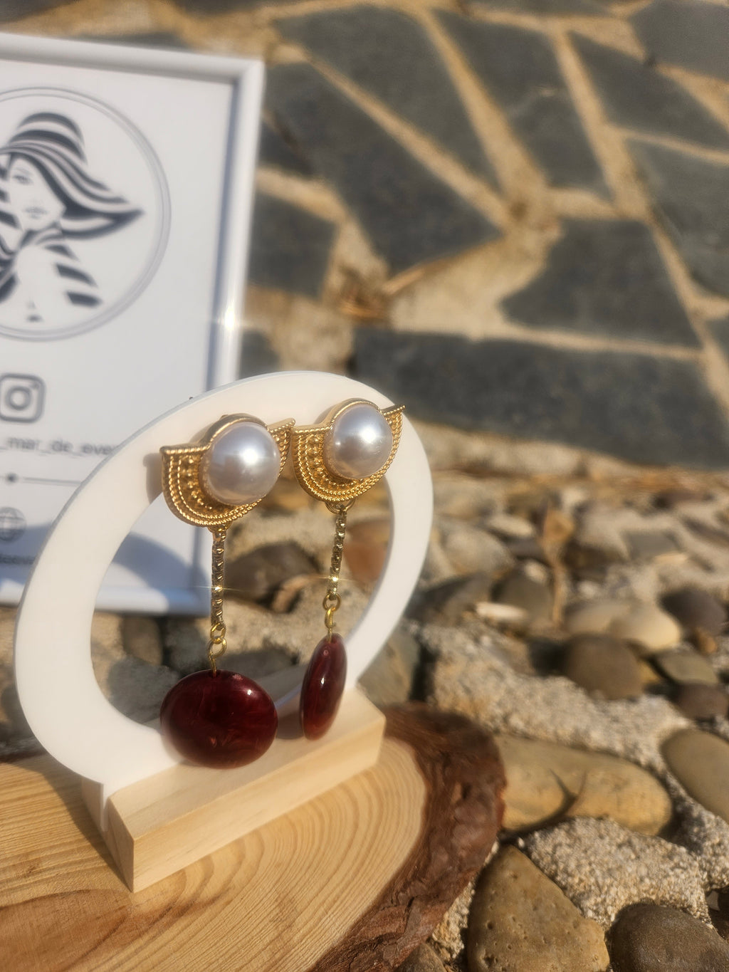 Pendientes colgantes con perlas blancas y gotas rojas sobre soporte de madera.