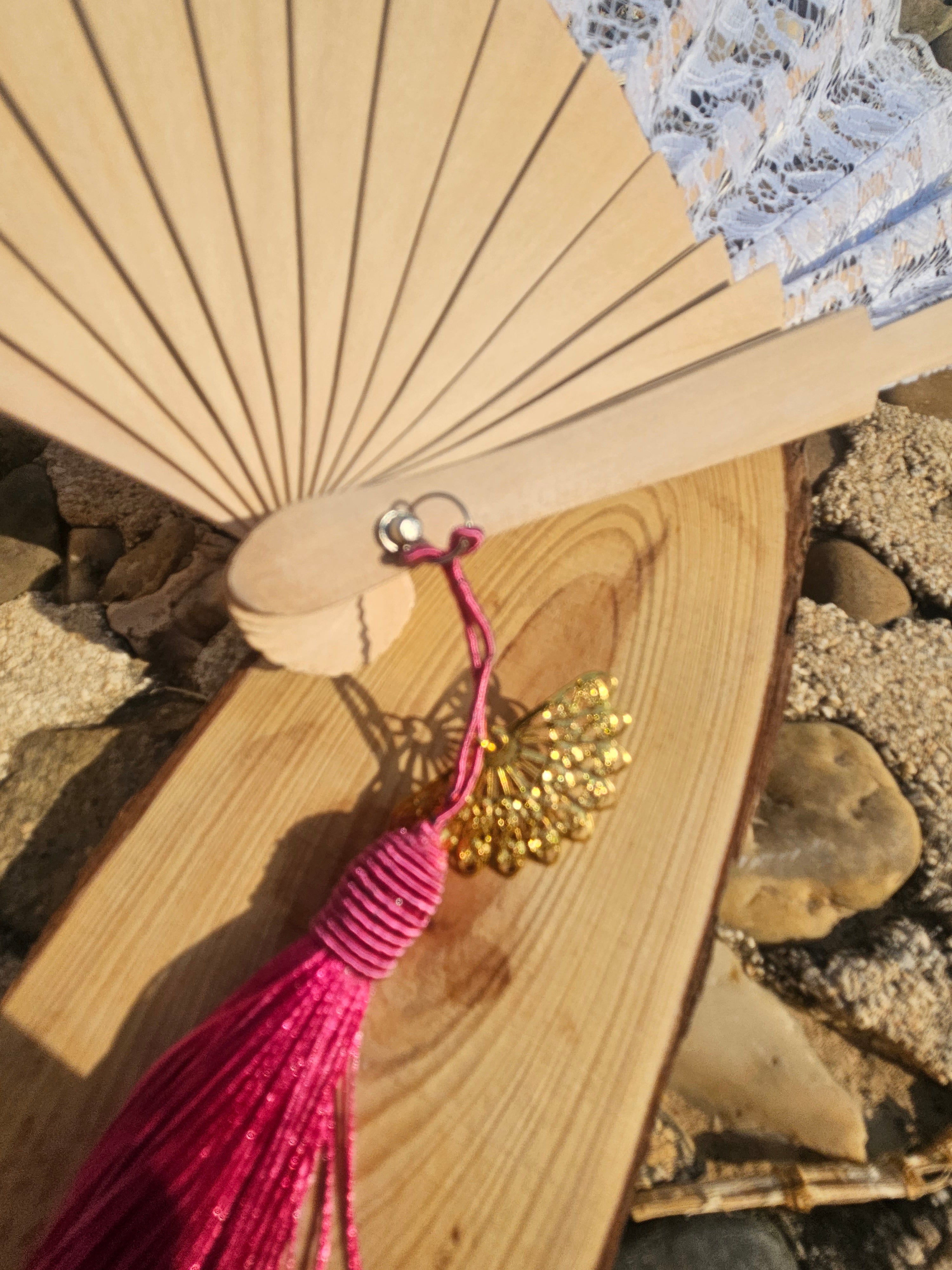 Abanico de madera con borla fucsia y colgante dorado, cerca del broche