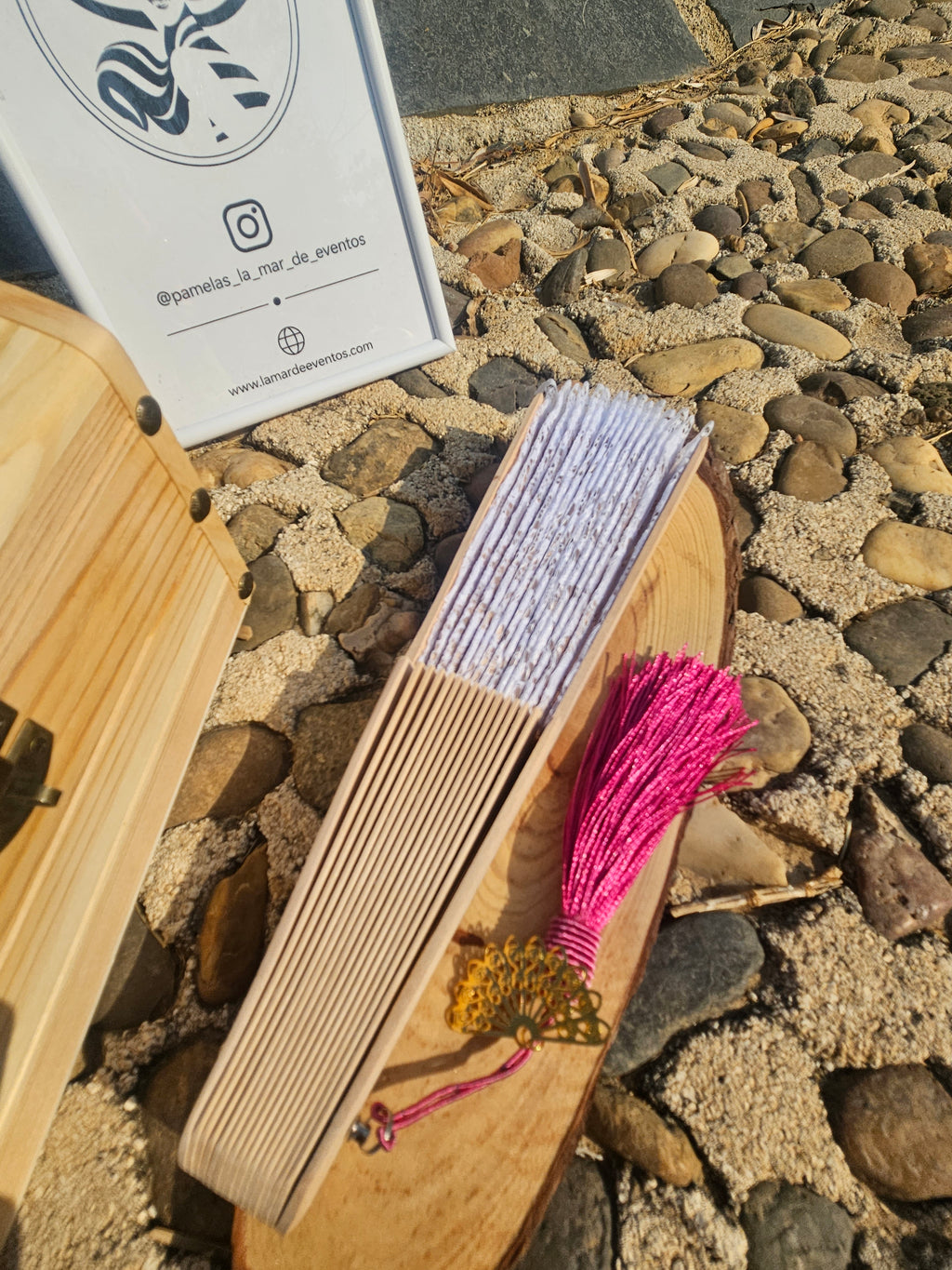 Abanico con varillas de madera y borla fucsia, junto a un estuche de regalo