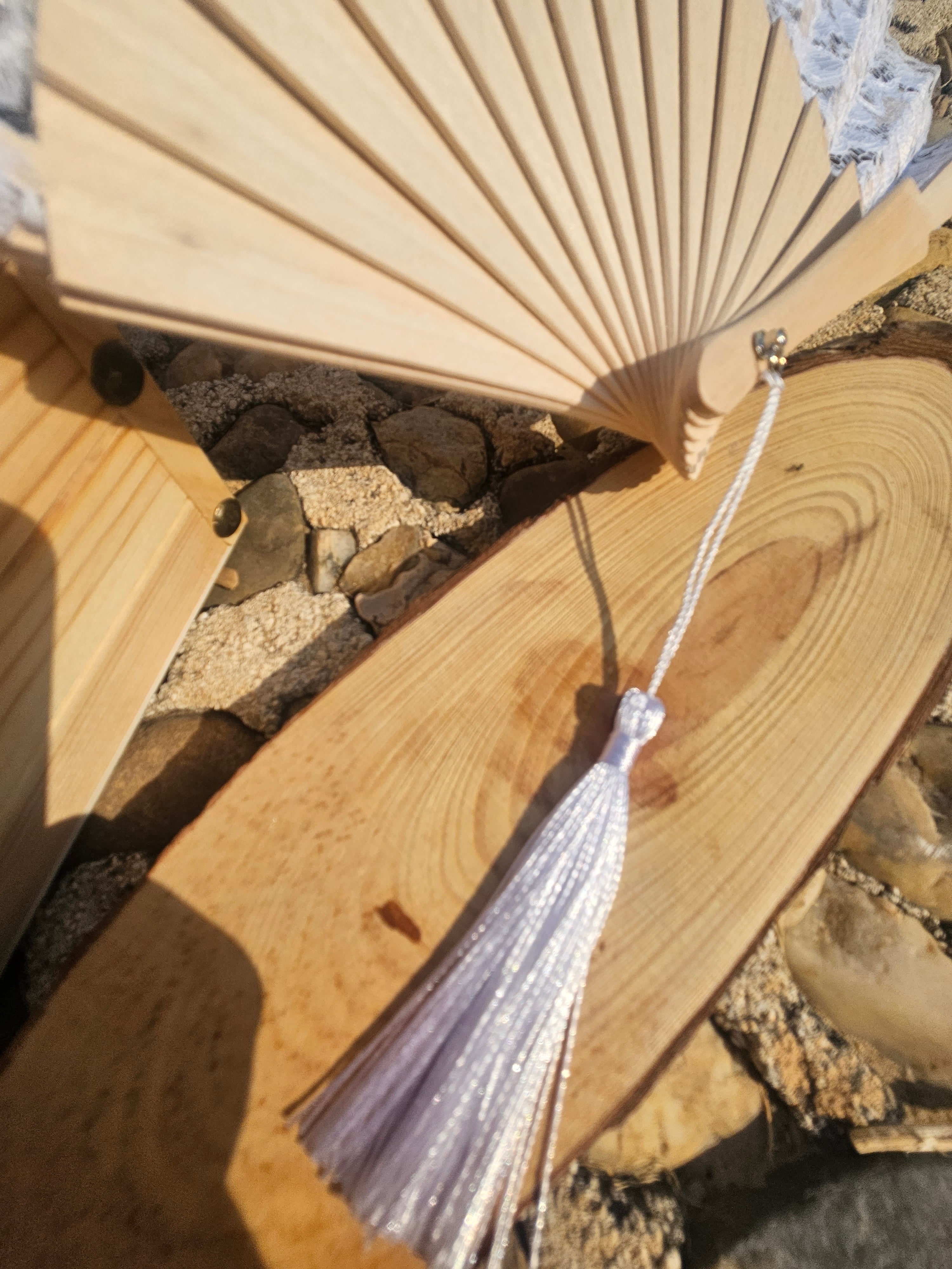 Abanico blanco de madera con encaje y borla plateada; enfoque en la borla.