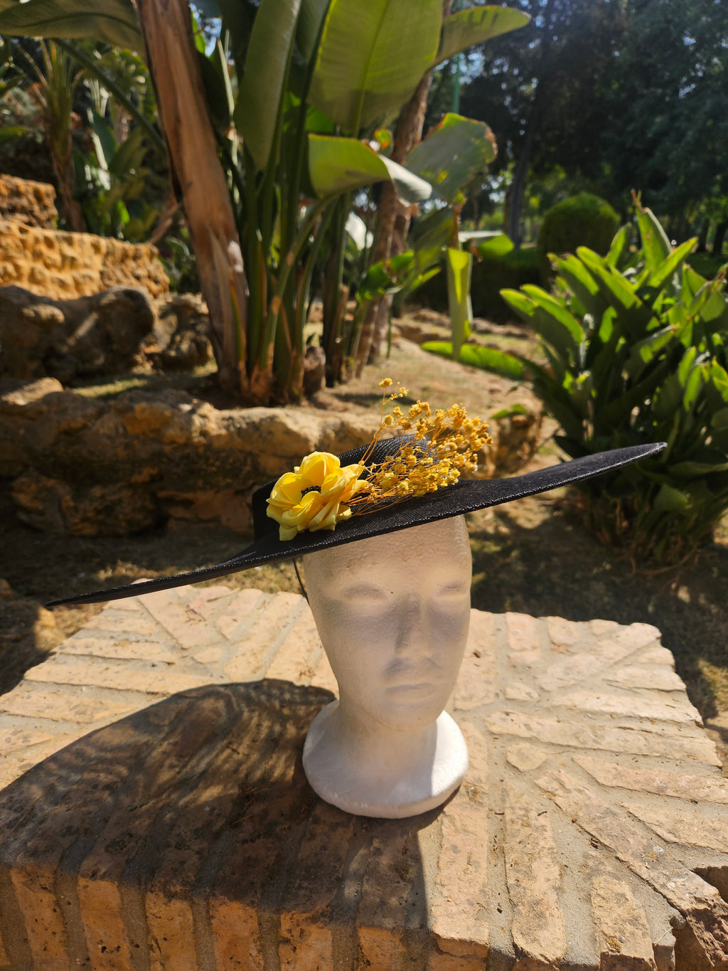 Sombrero de ala ancha negro con flores amarillas y ramitas doradas.