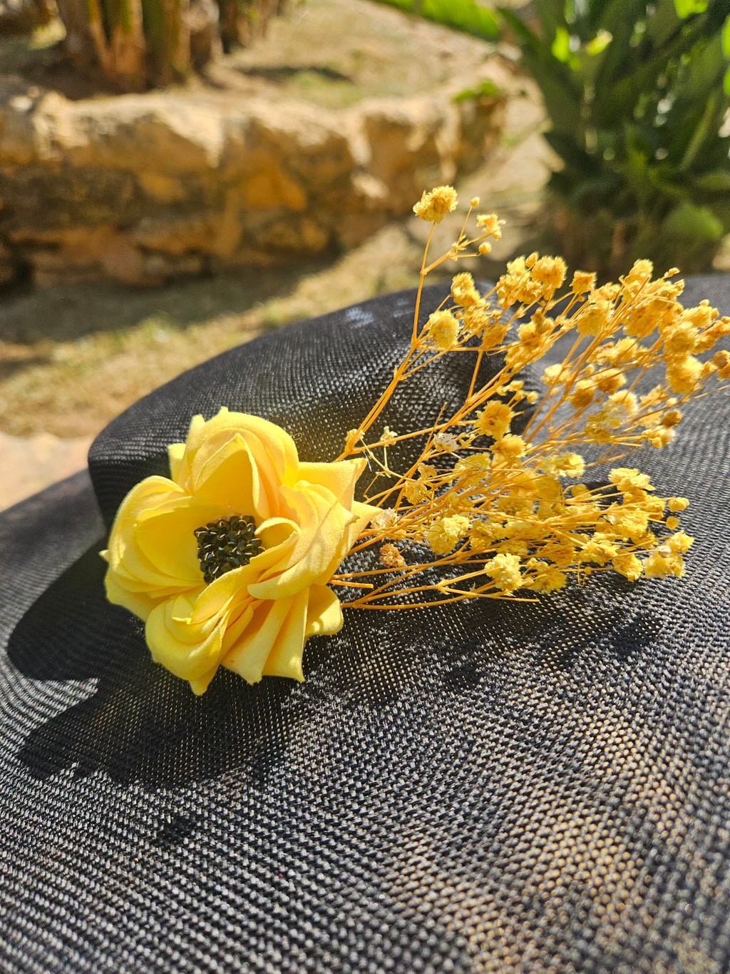 Sombrero negro de ala ancha con adorno floral amarillo sobre cinta textil.