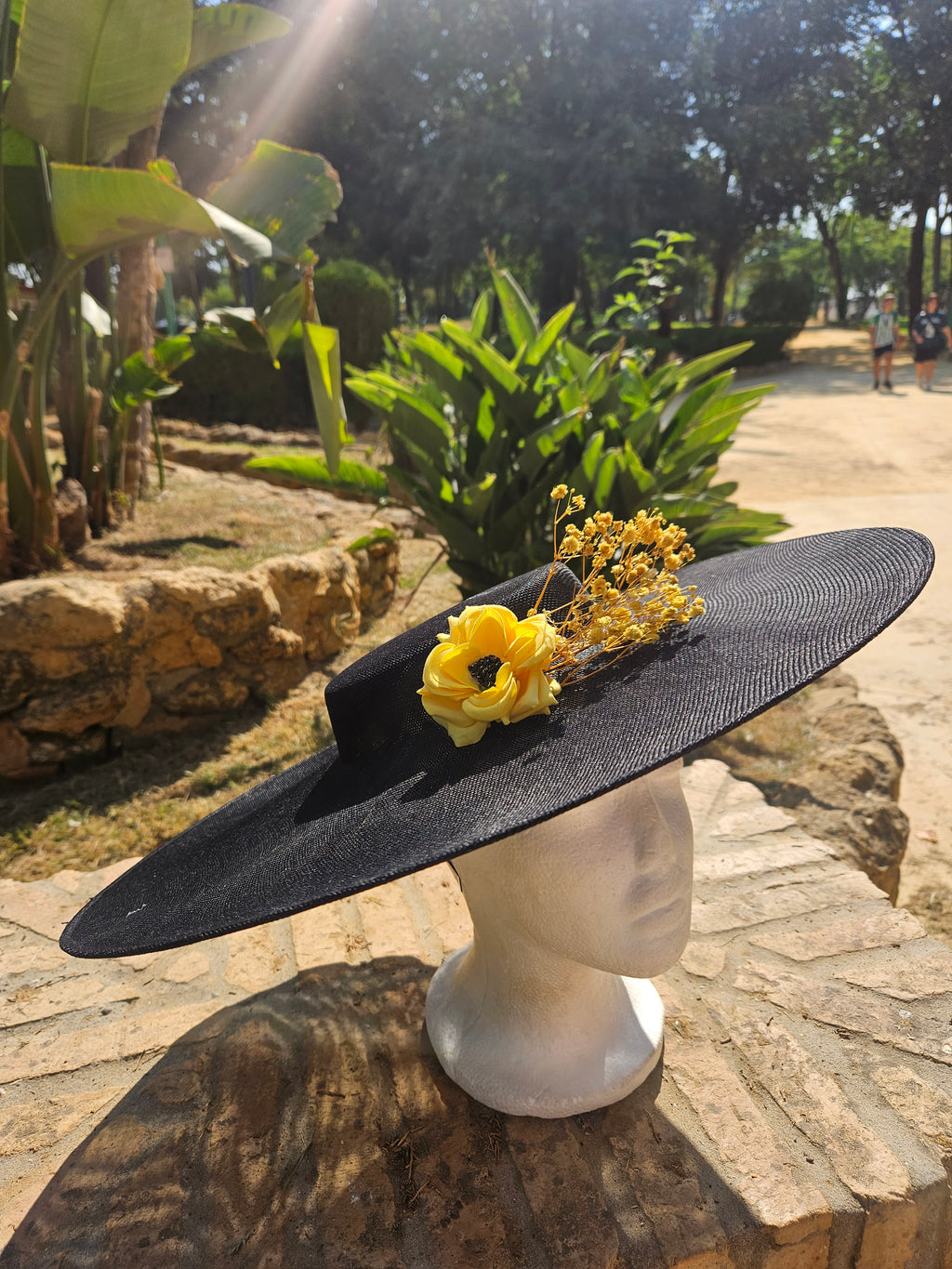 Sombrero de ala ancha negro con flor amarilla y ramitas doradas, vista lateral.