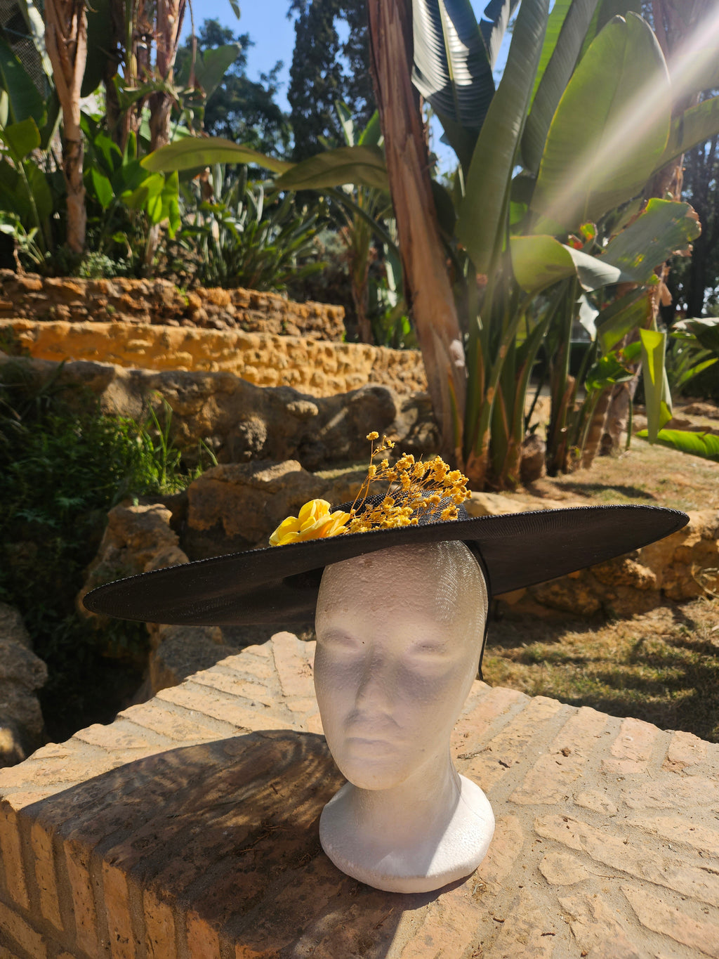 Sombrero de ala ancha negro con tocado floral amarillo, vista inclinada.