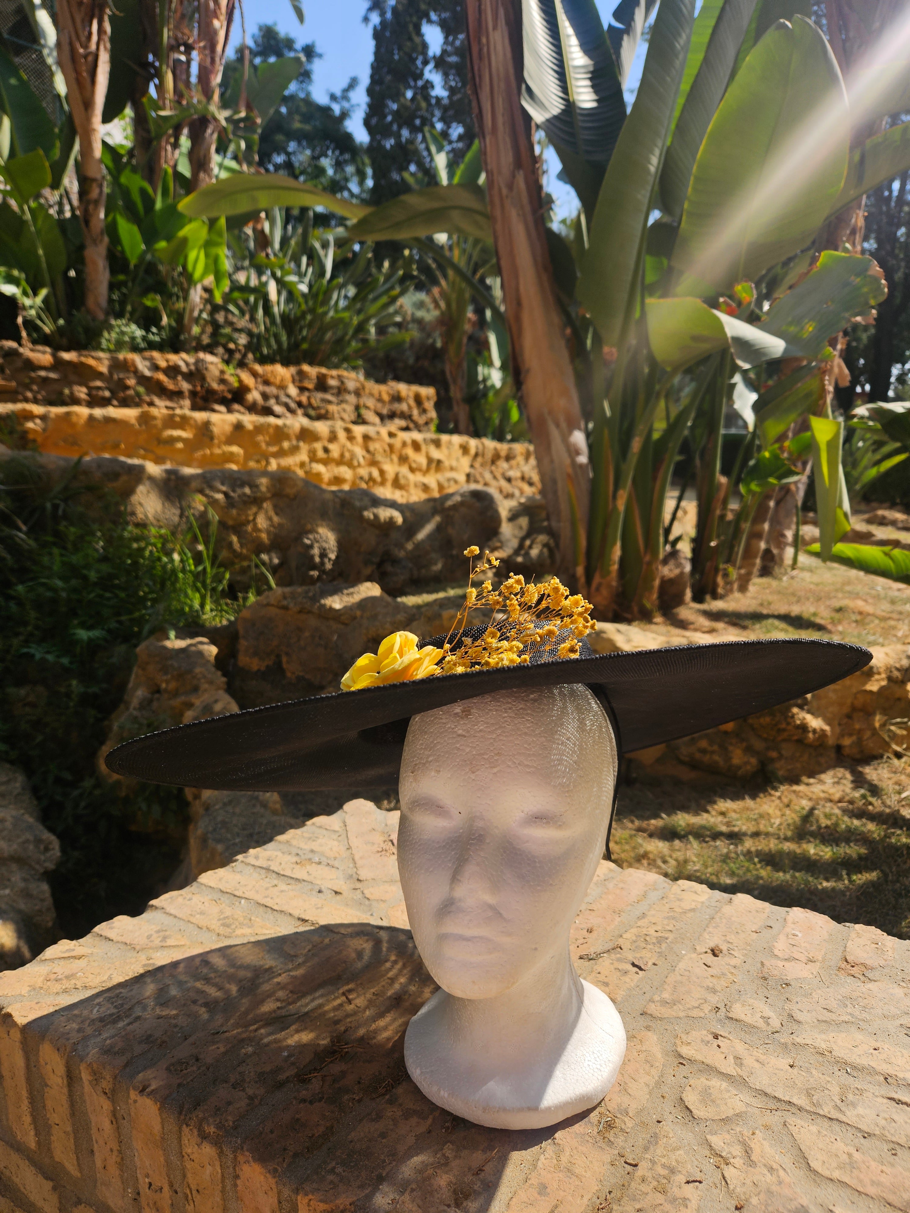 Sombrero de ala ancha negro con tocado floral amarillo, vista inclinada.