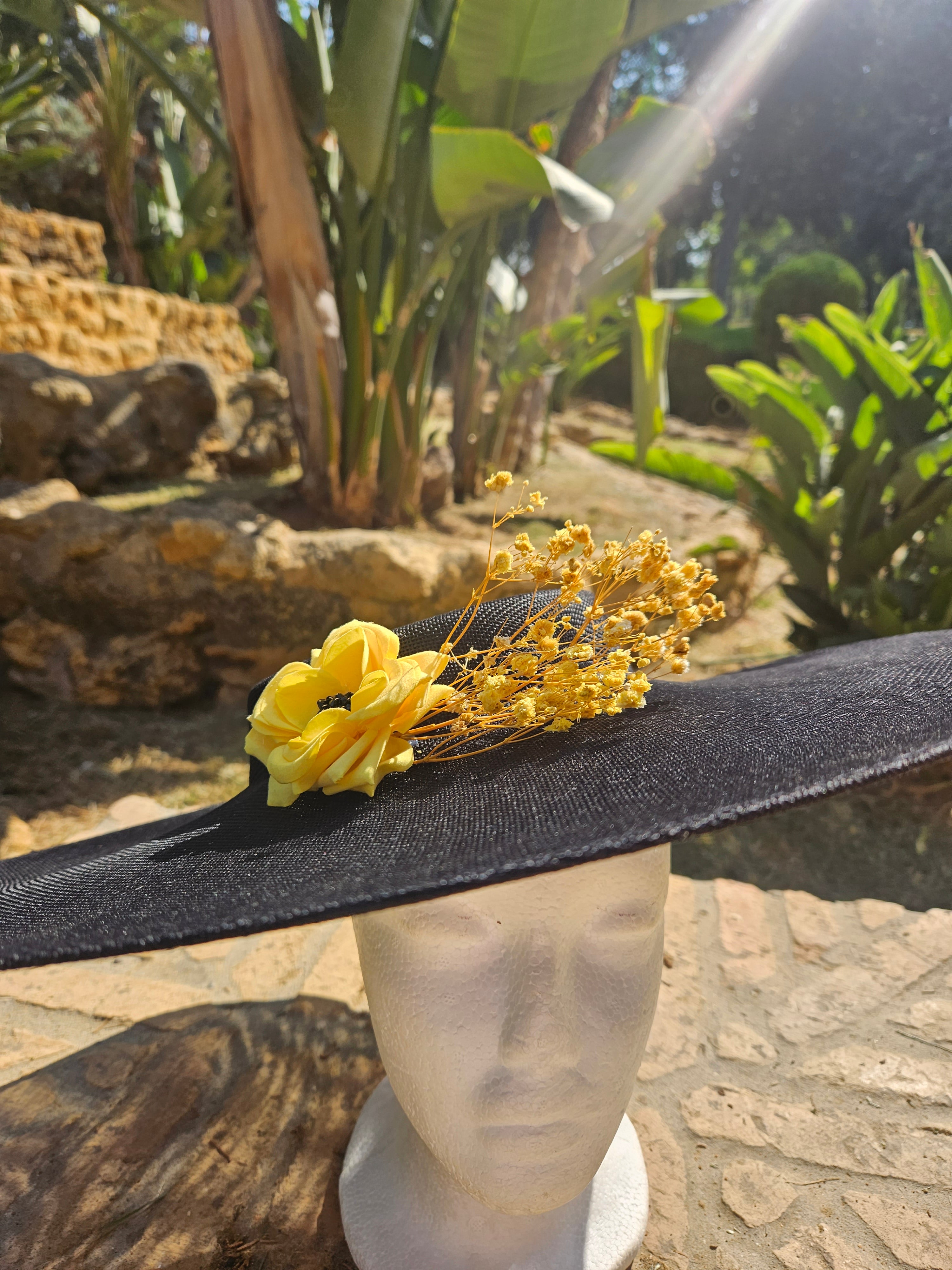 Sombrero de ala ancha negro con flor amarilla y pequeñas flores doradas, perfil.