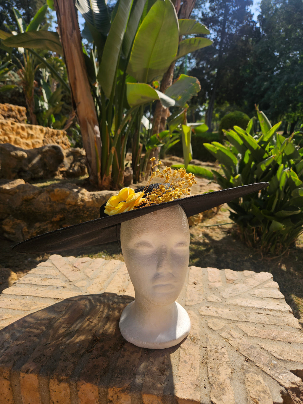 Sombrero de ala ancha negro con adorno floral amarillo y banda decorativa.