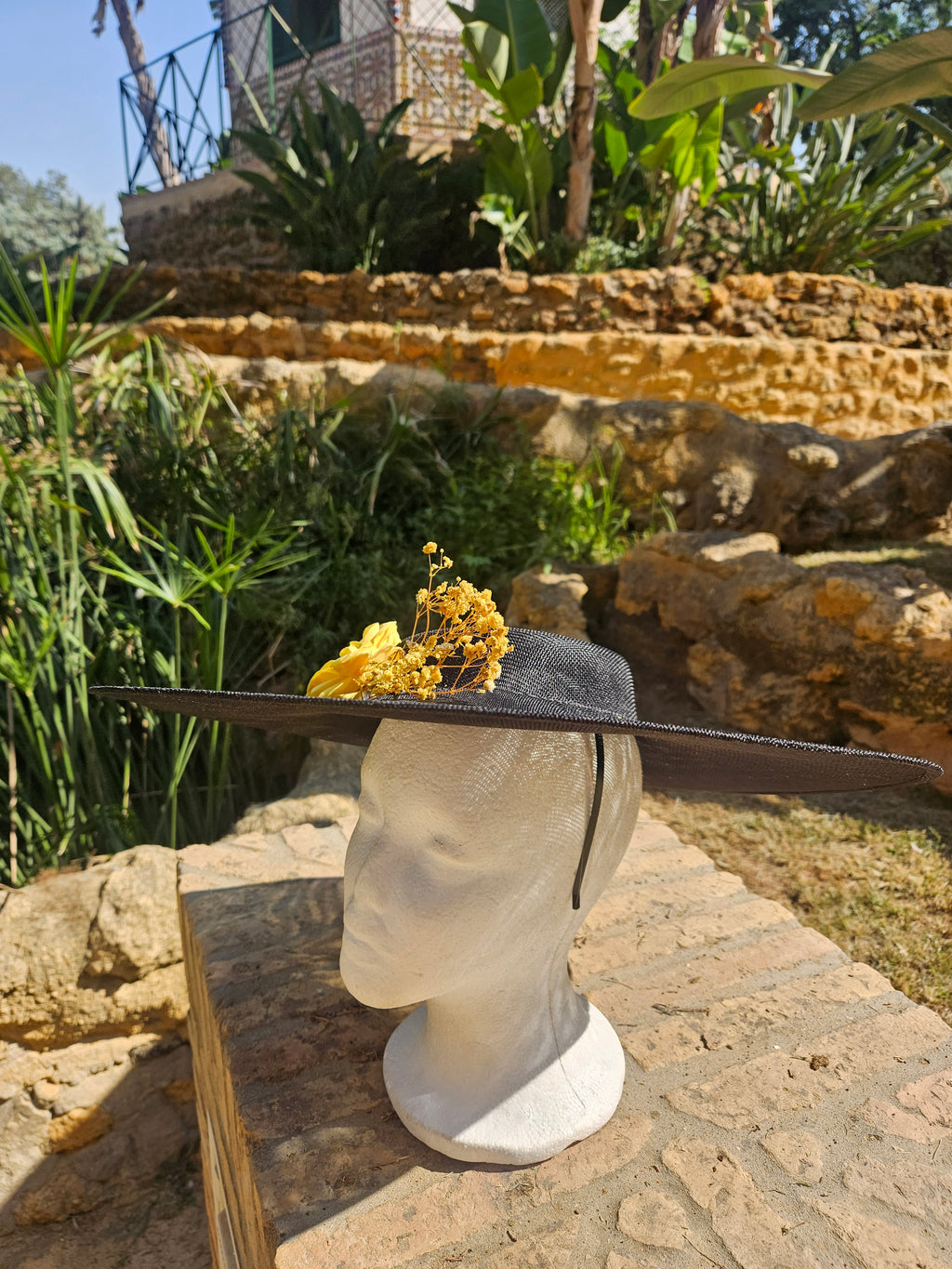 Sombrero de ala ancha negro con adorno floral amarillo, vista lateral.