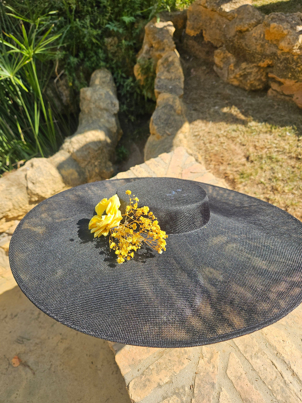 Sombrero negro de ala ancha con flor amarilla central y ramitas doradas.