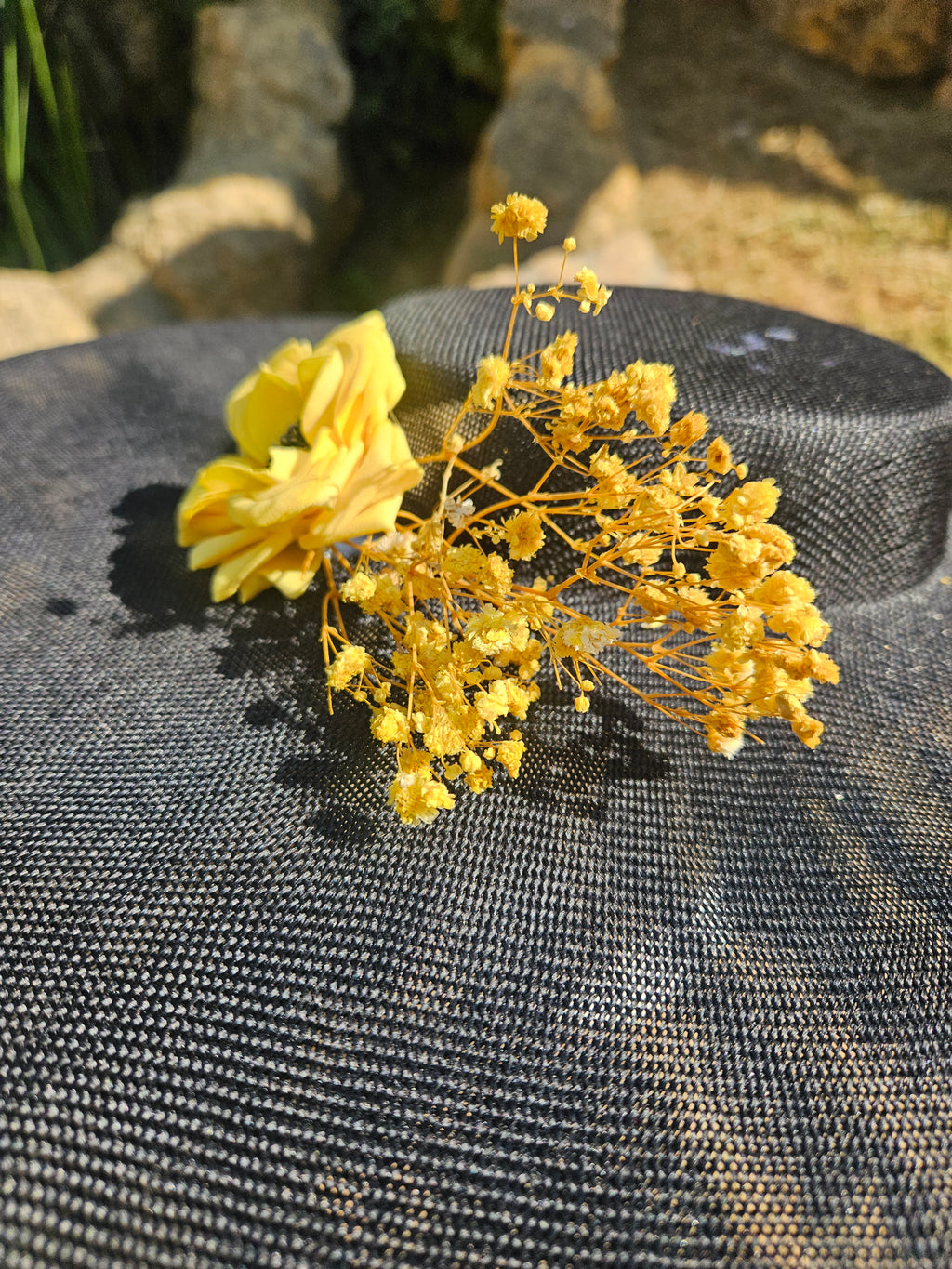 Sombrero de ala ancha negro con adorno floral amarillo y ramitas doradas, detalle.
