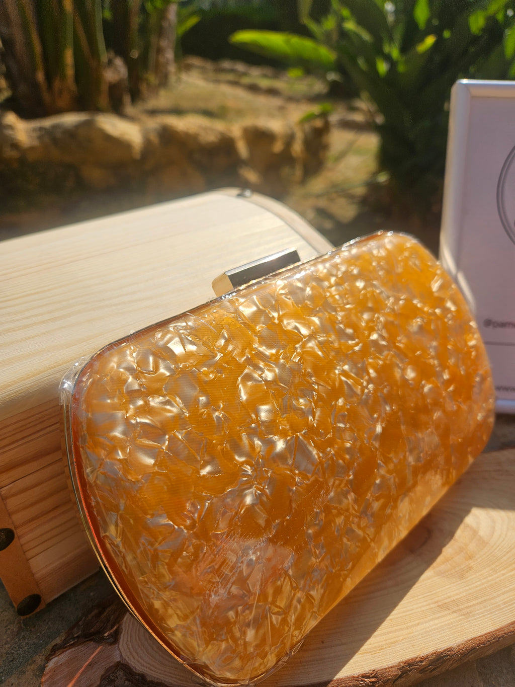 Bolso clutch ámbar con cierre rectangular metálico y textura transparente brillante