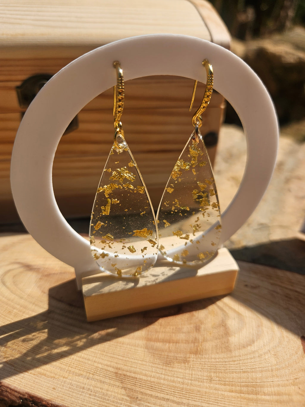 Pendientes de gota dorados con salpicaduras amarillas en soporte blanco circular.