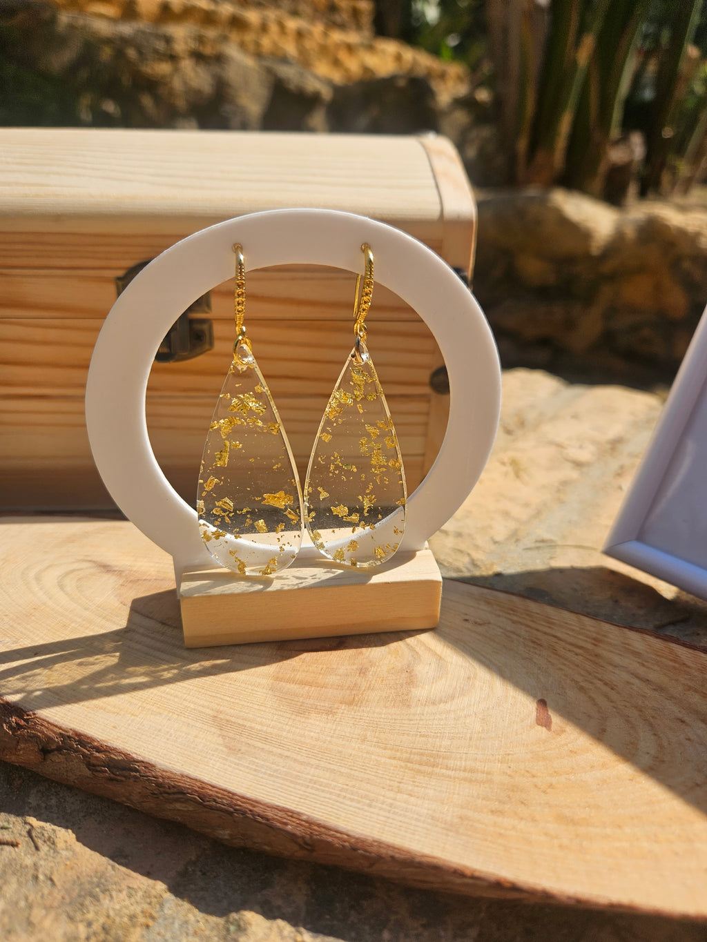 Pendientes de gota dorados con purpurina amarilla en soporte blanco, vista frontal.