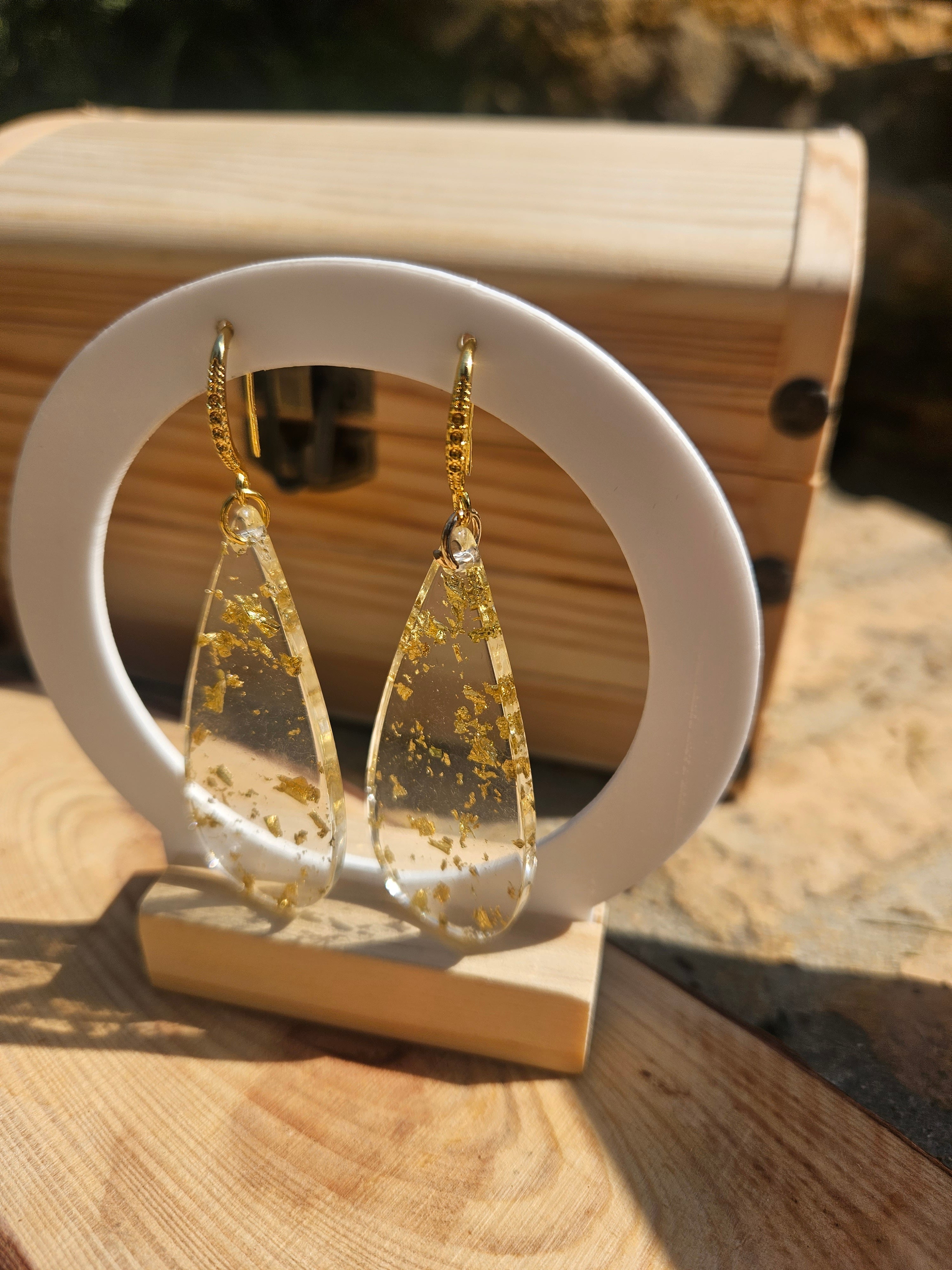 Pendientes de gota dorados con salpicaduras, sobre soporte blanco con base de madera.