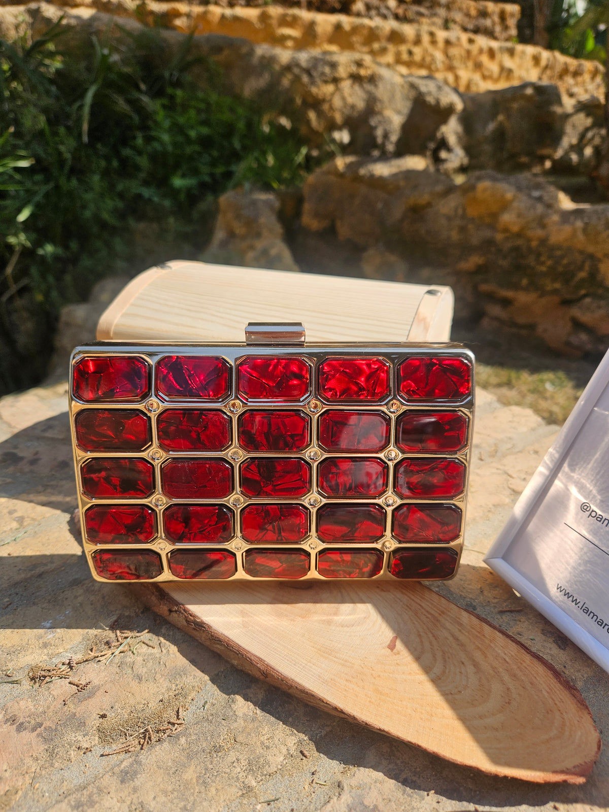 Bolso tipo caja con panel rojo cuadriculado y broche metálico sobre tapa de madera