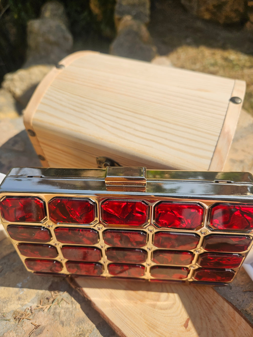 Bolso tipo caja de madera clara con broche metálico y panel rojo de rombos