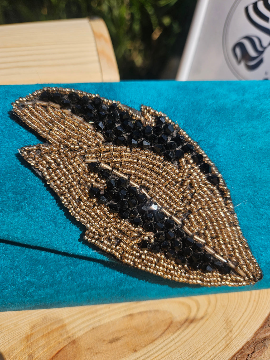 Bolso turquesa de solapa con bordado detallado tipo ojo en tonos dorados y negros