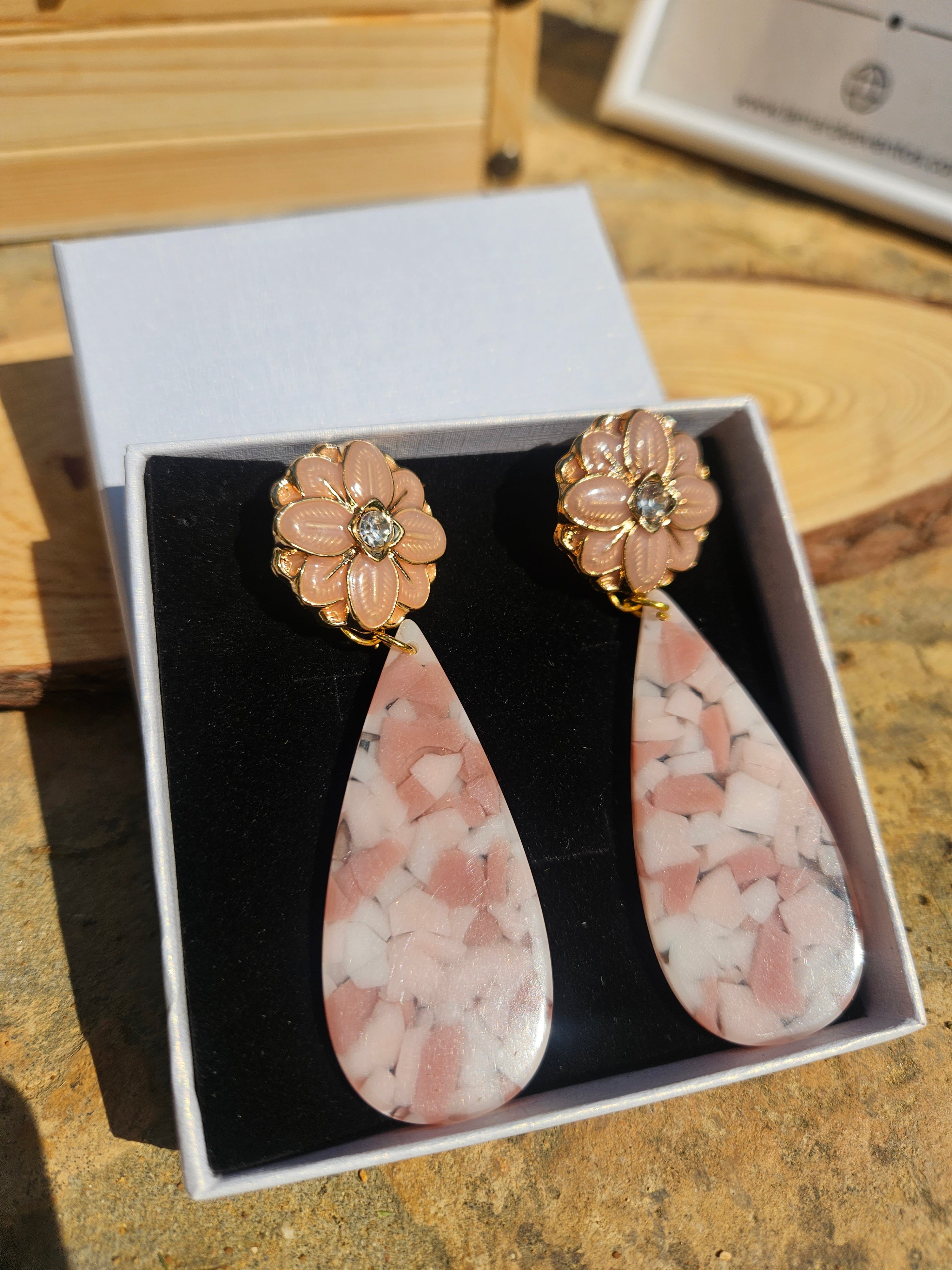 Pendientes con flores doradas y gota rosa jaspeada, presentados en estuche negro.
