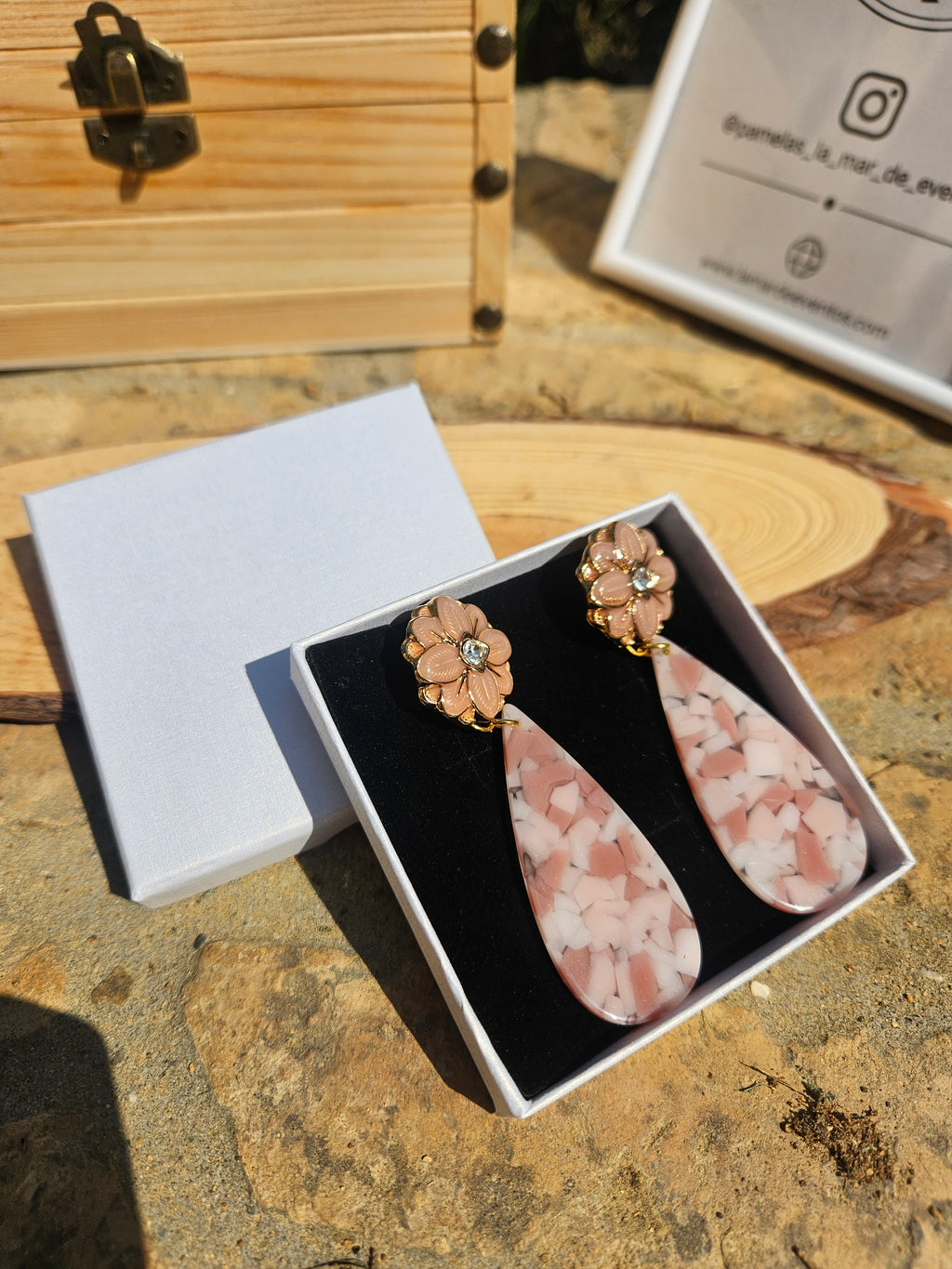 Pendientes en estuche abierto: flores doradas y gota rosa con efecto jaspeado.