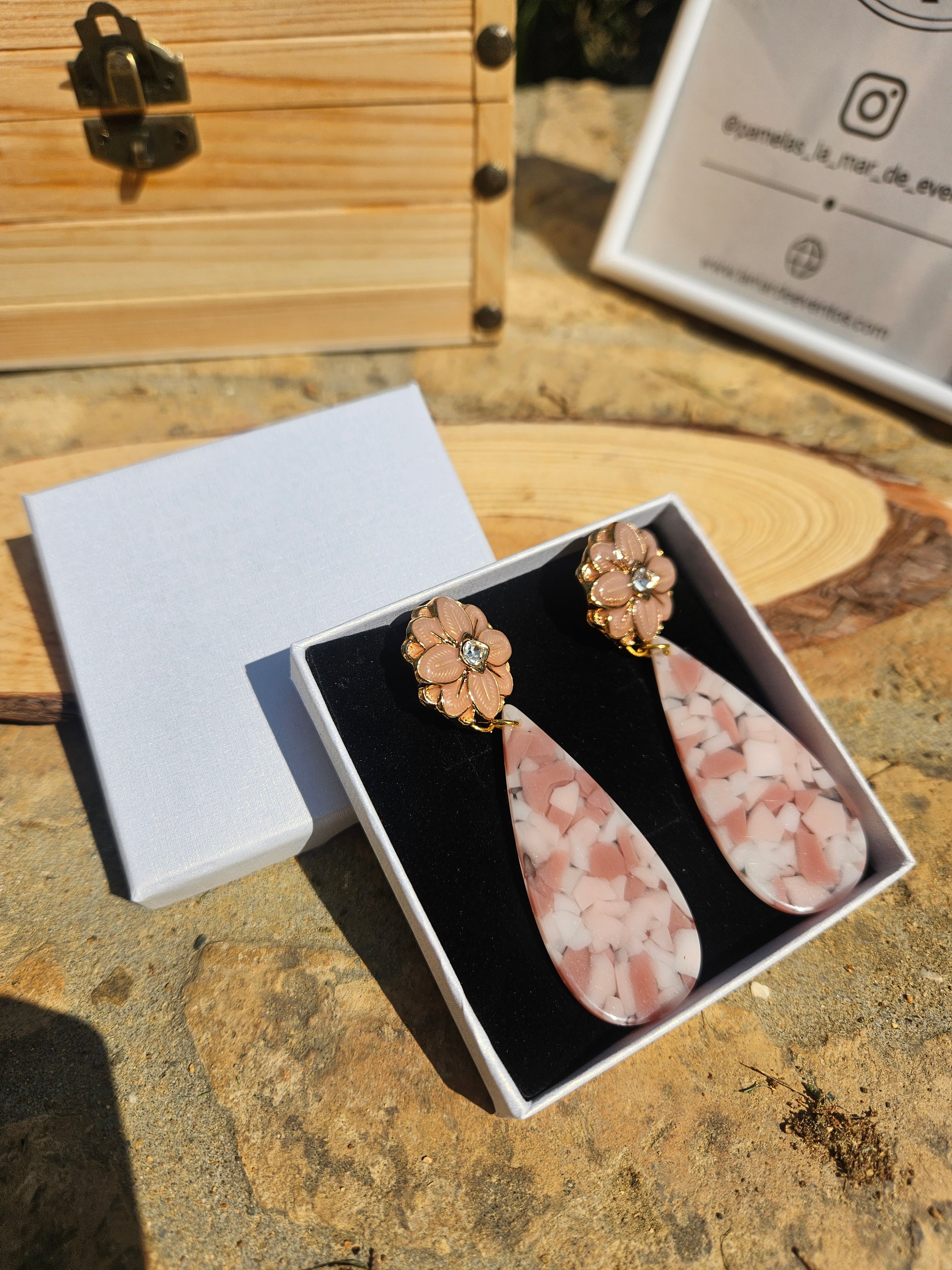Pendientes en estuche abierto: flores doradas y gota rosa con efecto jaspeado.