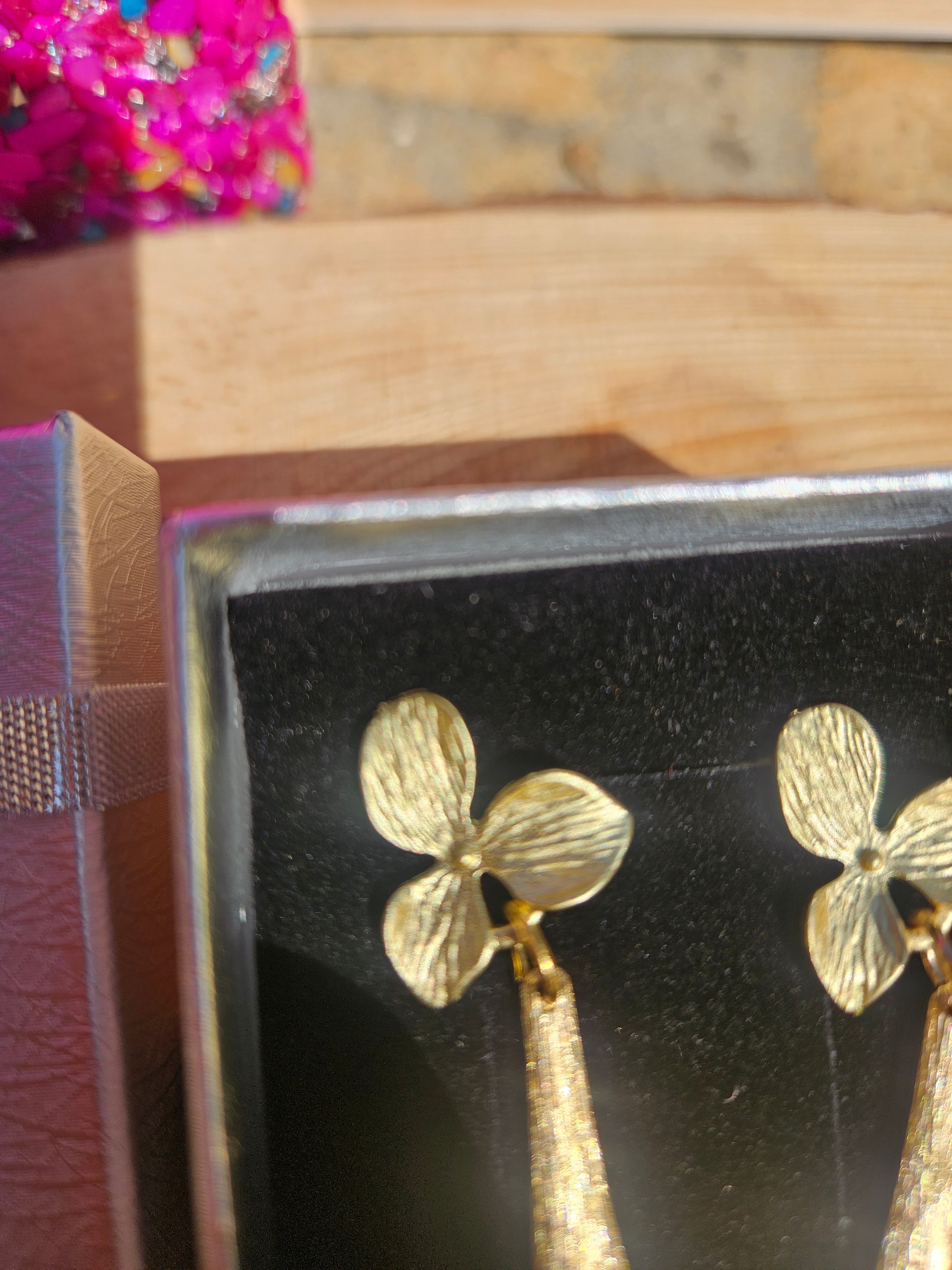 Pendientes dorados con flor y dos colgantes tipo gota, vista lateral en caja
