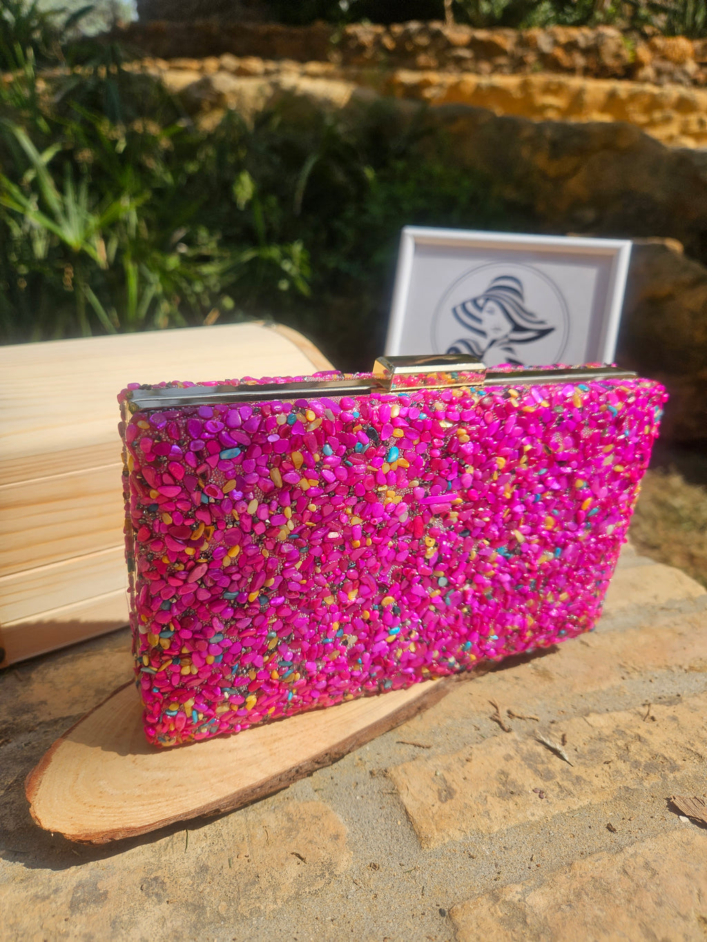 Bolso tipo cartera con marco de madera clara y pedrería rosa intensa, perfil