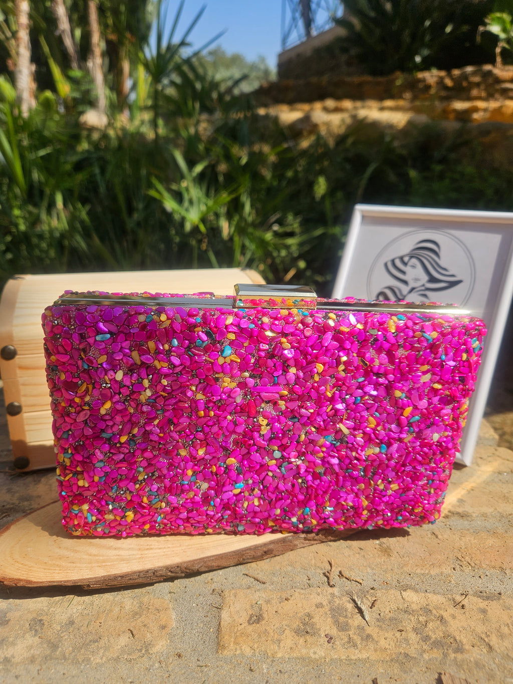 Bolso tipo clutch de pedrería magenta con bordes de madera clara, vista de frente