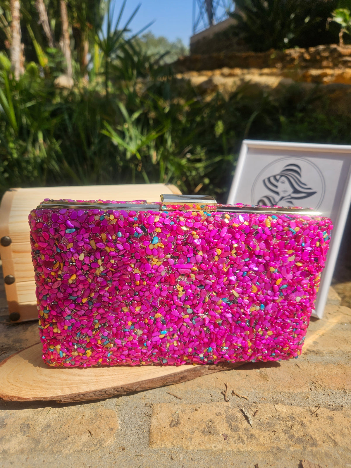 Bolso tipo clutch de pedrería magenta con bordes de madera clara, vista de frente